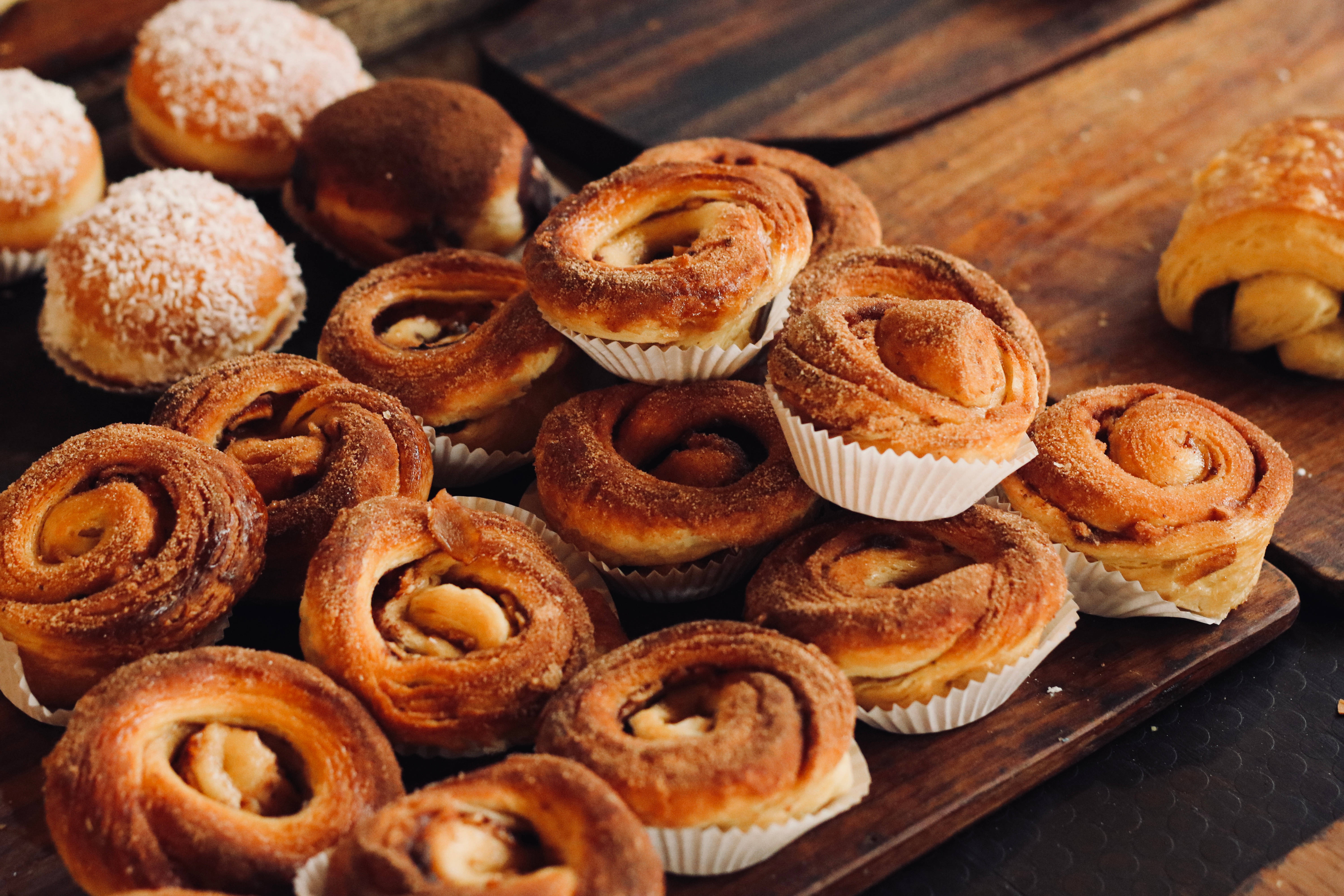 Pastry 桌布 壁紙 — 金黃色的肉桂捲和椰子甜甜圈誘人地堆疊在質樸的木托盤上。