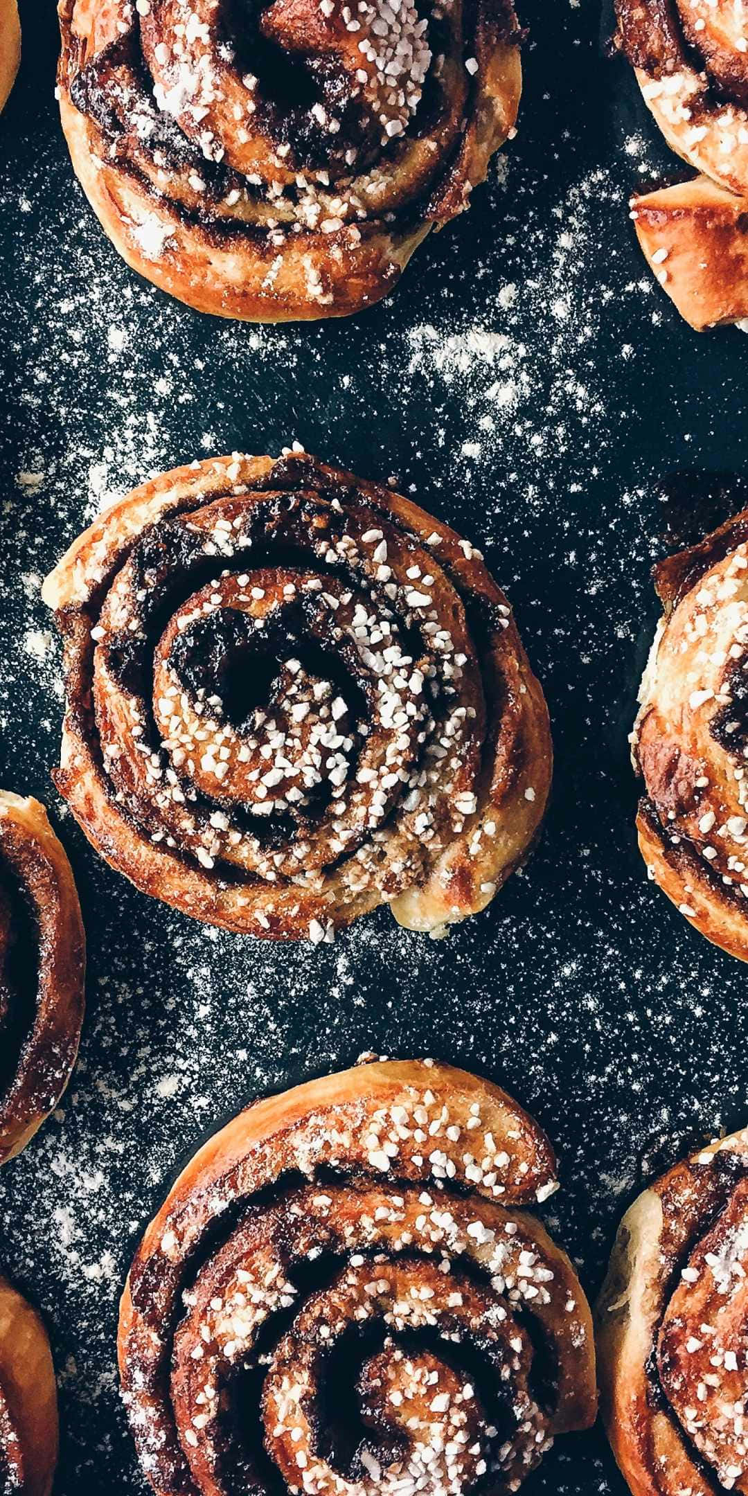 Pastries 桌布 壁紙 — 金黃色的肉桂捲撒上糖，放在深色撒粉的表面上，以俯拍特寫鏡頭拍攝。