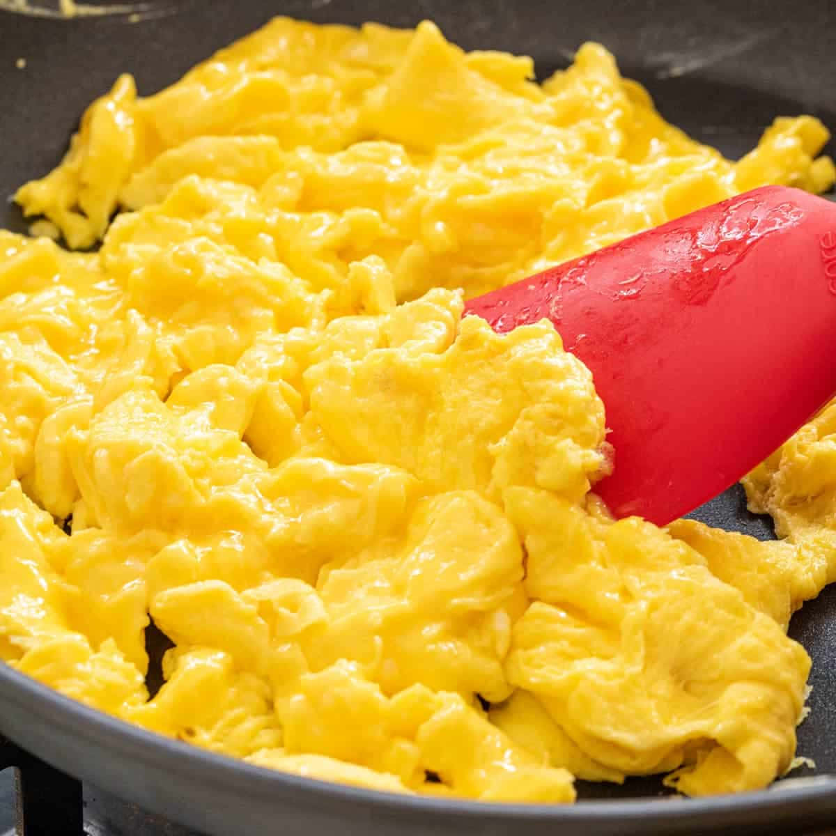 Scrambled Egg 桌布 壁紙 — 金黃色的蓬鬆炒蛋在黑色平底鍋中用紅色矽膠鍋鏟攪拌。