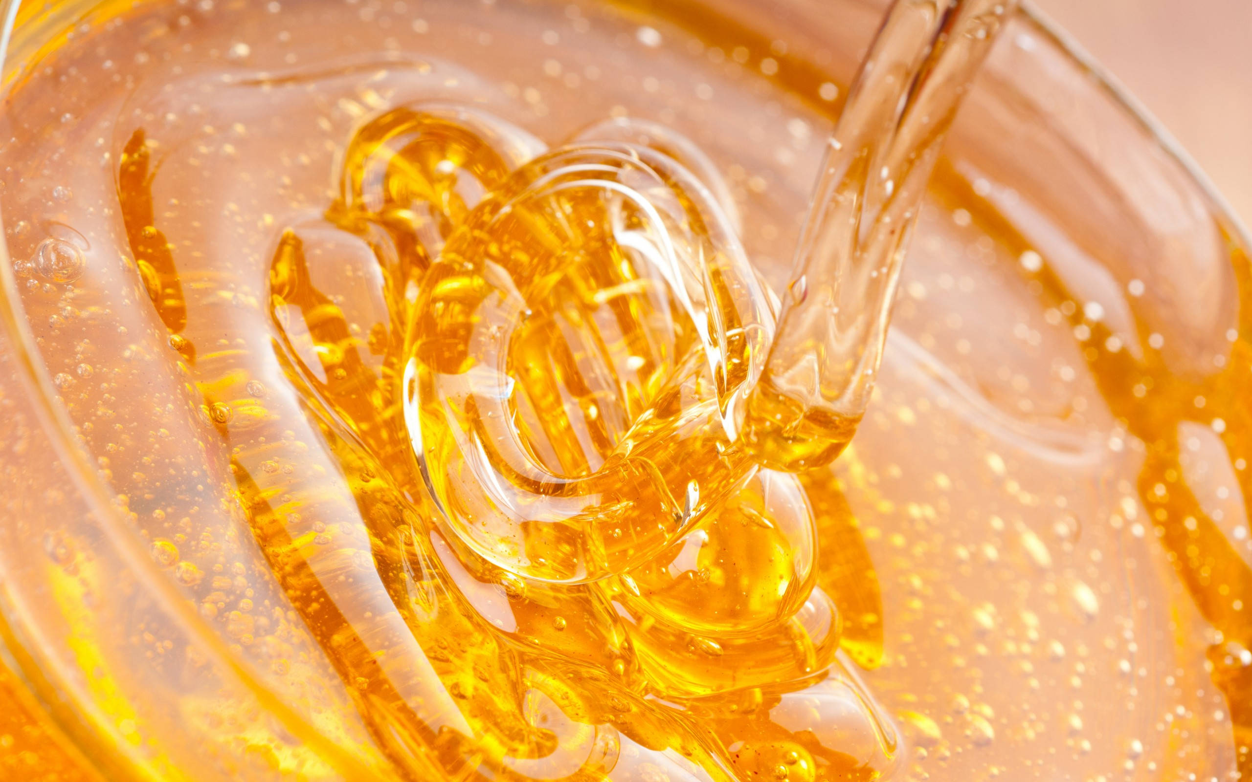 honey 桌布 壁紙 — 金黃色的蜂蜜以濃稠黏滯的流動形成漩渦圖案，帶有閃閃發光的滴珠和氣泡。