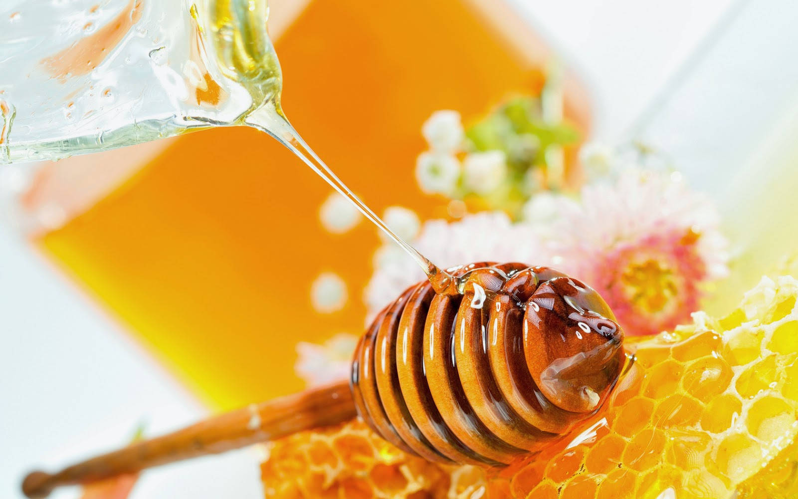 Honeycomb 桌布 壁紙 — 金黃色的蜂蜜從勺子滴到蜂巢上，旁邊有柔和的粉紅色花朵和一個玻璃罐。