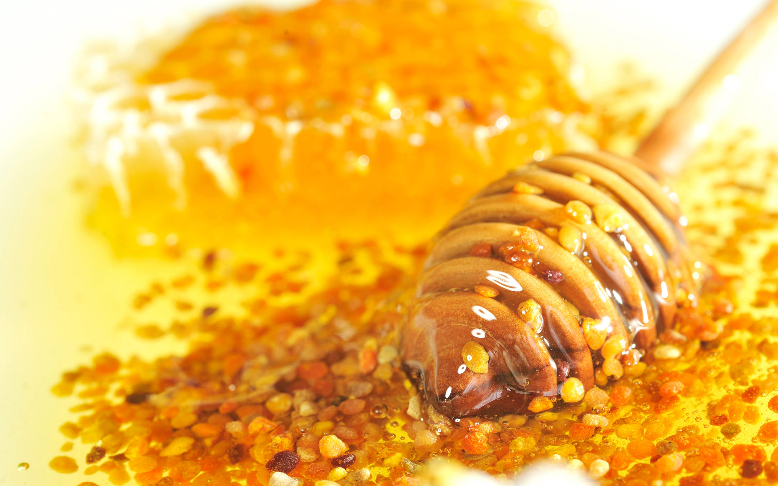 Honeycomb 桌布 壁紙 — 金黃色的蜂蜜從木勺滴落到蜂巢上，花粉斑點在柔和光線下閃閃發光。
