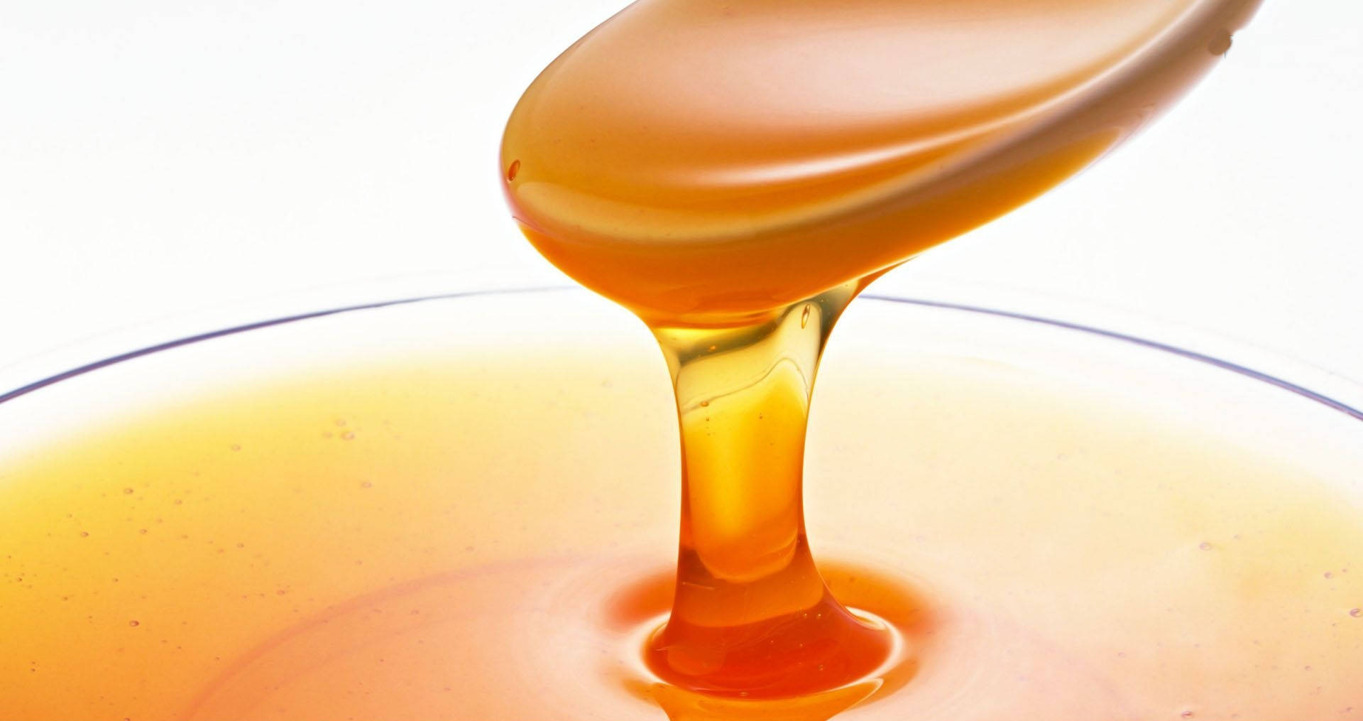 honey 桌布 壁紙 — 金黃色的蜂蜜從湯匙濃稠地流進玻璃碗中，背景是明亮的白色。