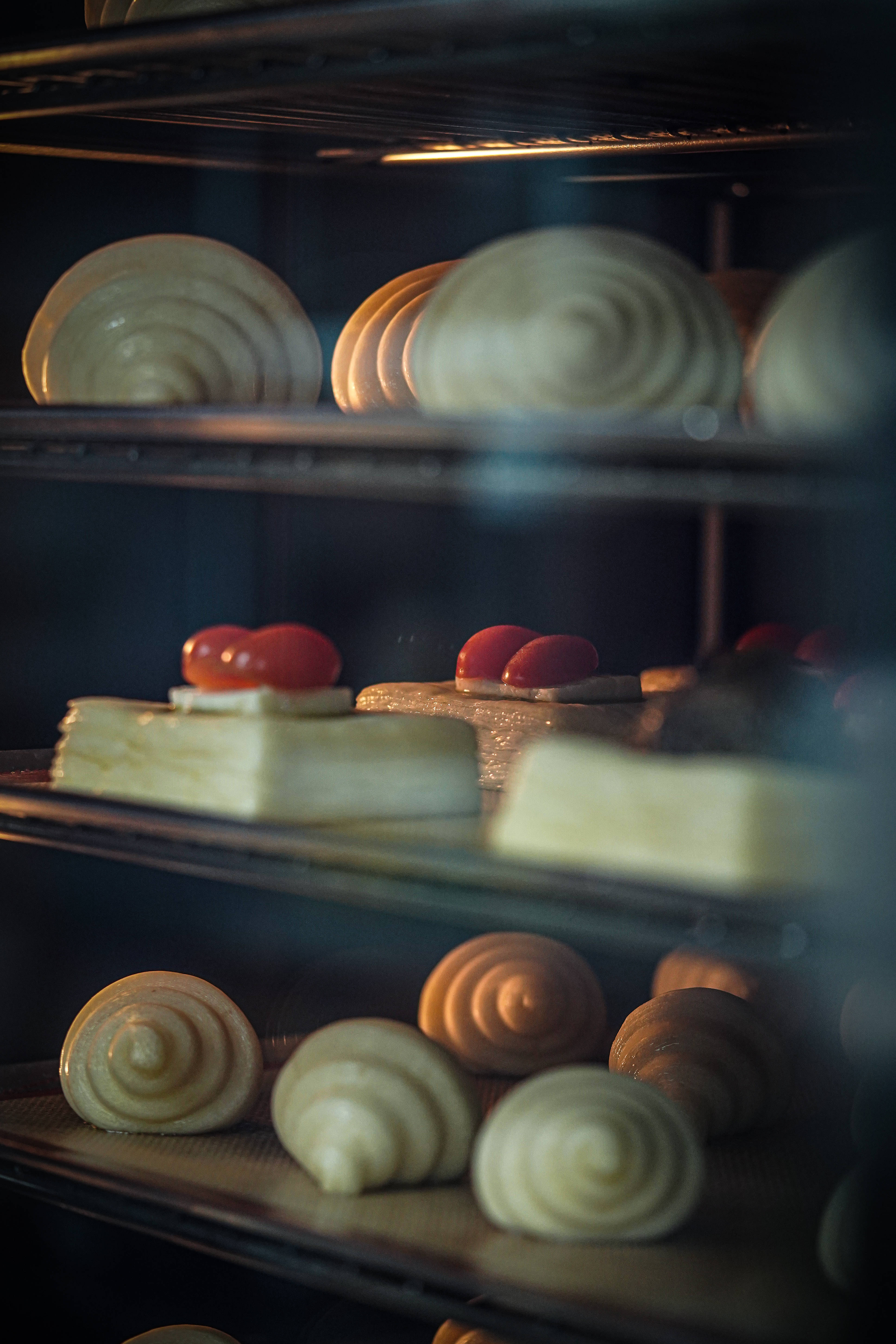 Pastries 桌布 壁紙 — 金黃色的螺旋糕點和櫻桃頂蛋糕在溫暖發光的烤箱中烘烤，具有柔和的焦點深度。