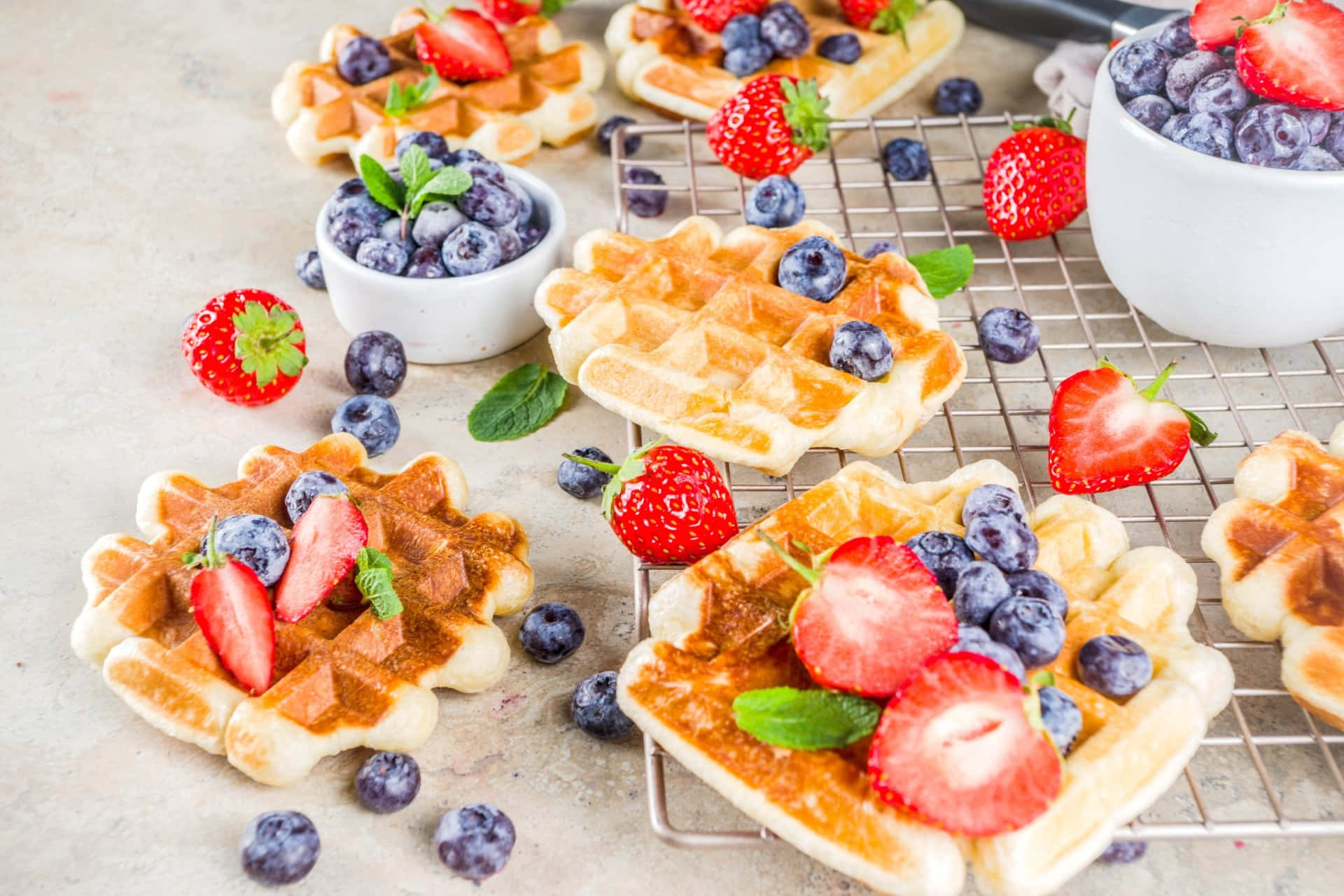 Waffle 桌布 壁紙 — 金黃色的鬆餅，上面放著新鮮草莓、藍莓和薄荷葉，在金屬架上冷卻。