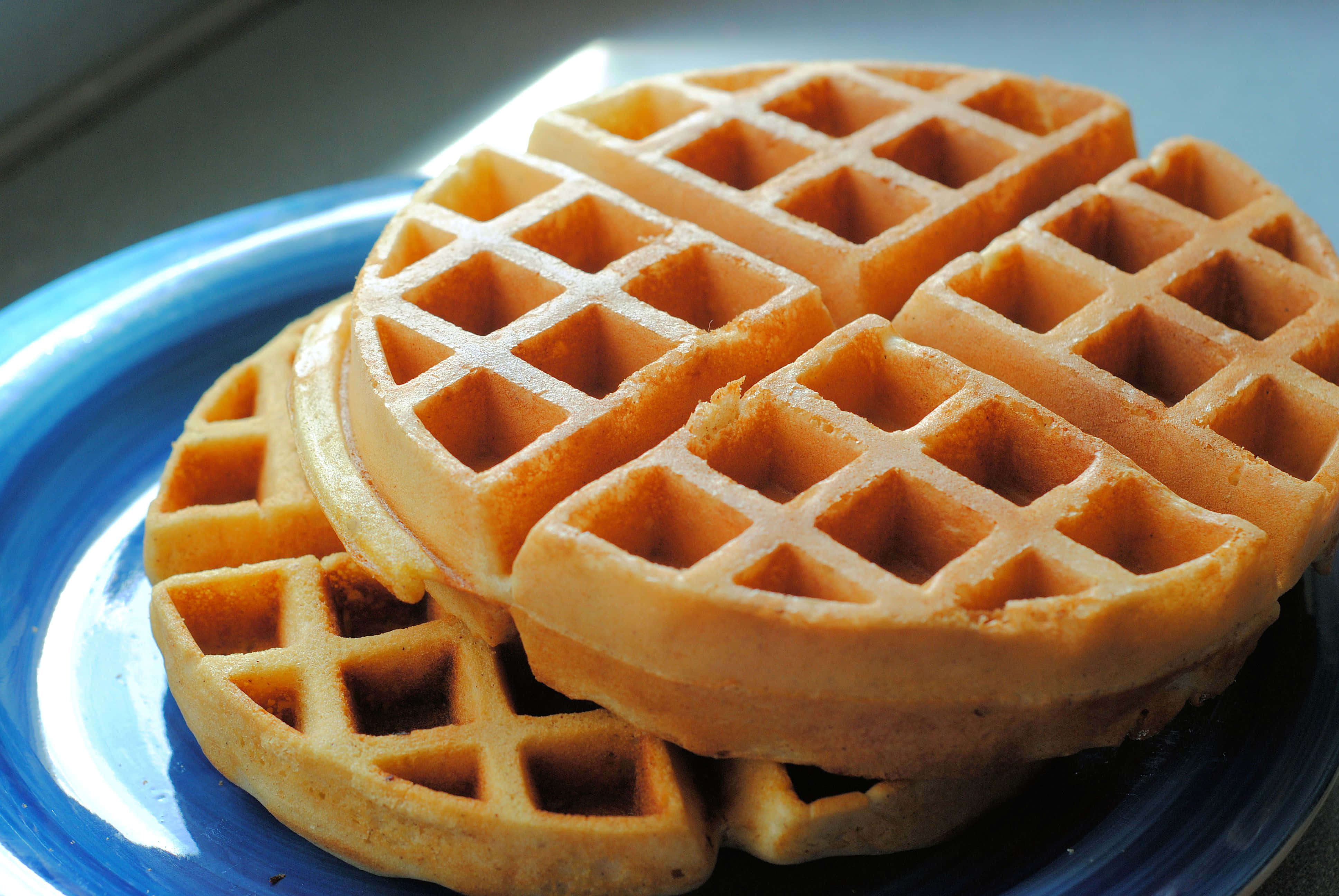 Waffle 桌布 壁紙 — 金黃色的鬆餅疊放在鮮藍色的盤子上，柔和晨光突顯其酥脆質感。
