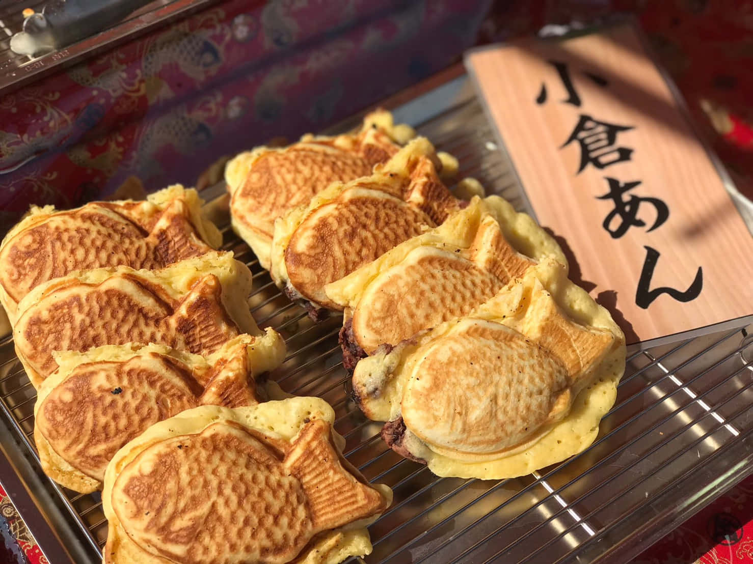 Japanese Sweets 桌布 壁紙 — 金黃色的魚形鯛魚燒，內餡是甜紅豆沙，放在金屬架上，旁邊有一個寫著日文字的木牌。