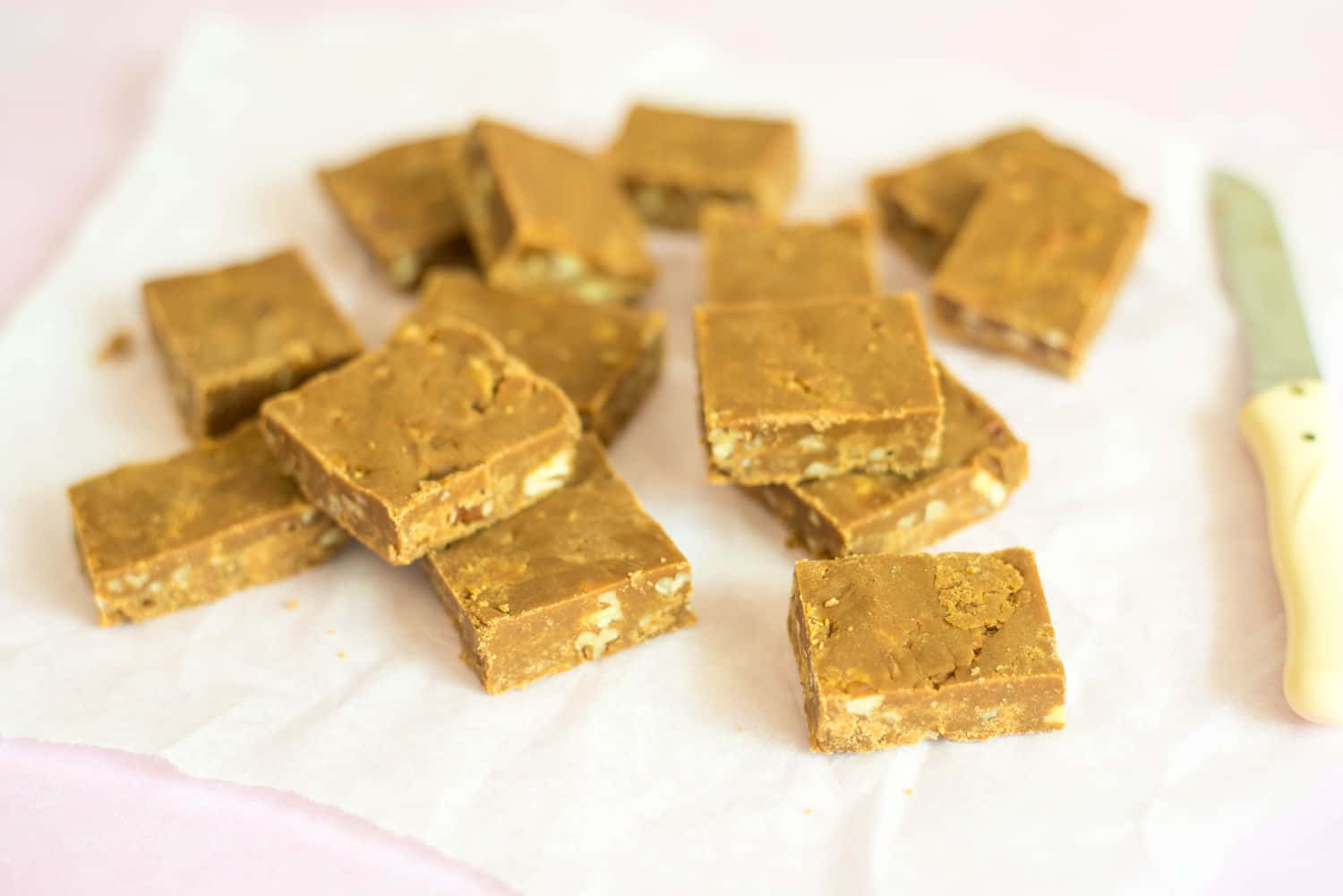 Penuche Fudge 桌布 壁紙 — 金黃色花生醬軟糖方塊，可見堅果，放在白色烘焙紙上，旁邊有一把淡黃色手柄的刀。