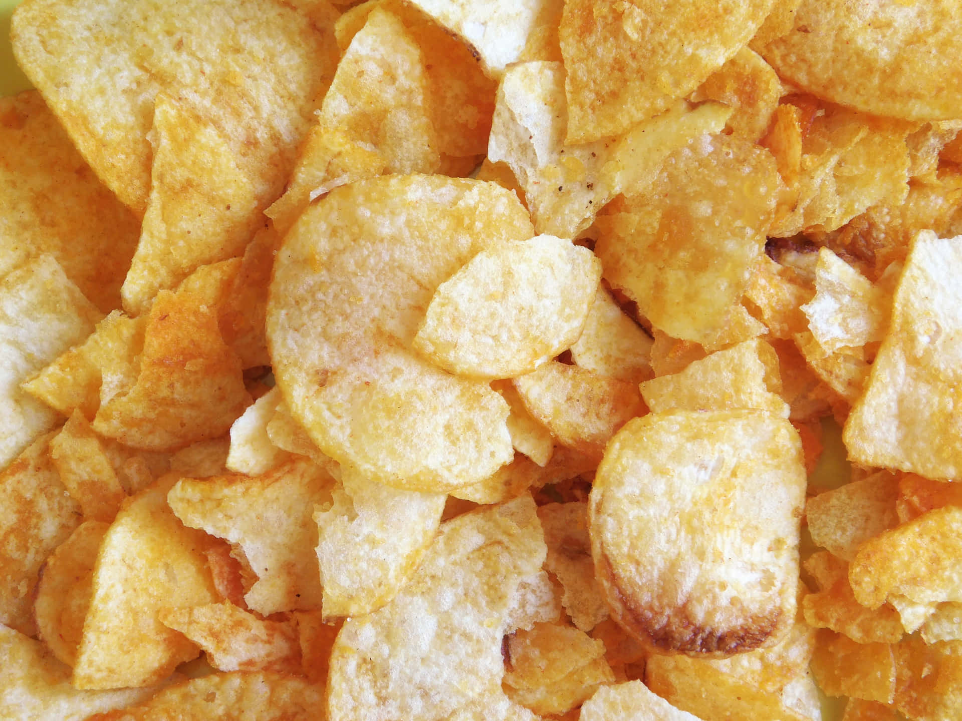 Chips texture 壁紙 — 金黃色薯片的特寫，具有酥脆質地和鹽晶體在明亮燈光下閃爍。