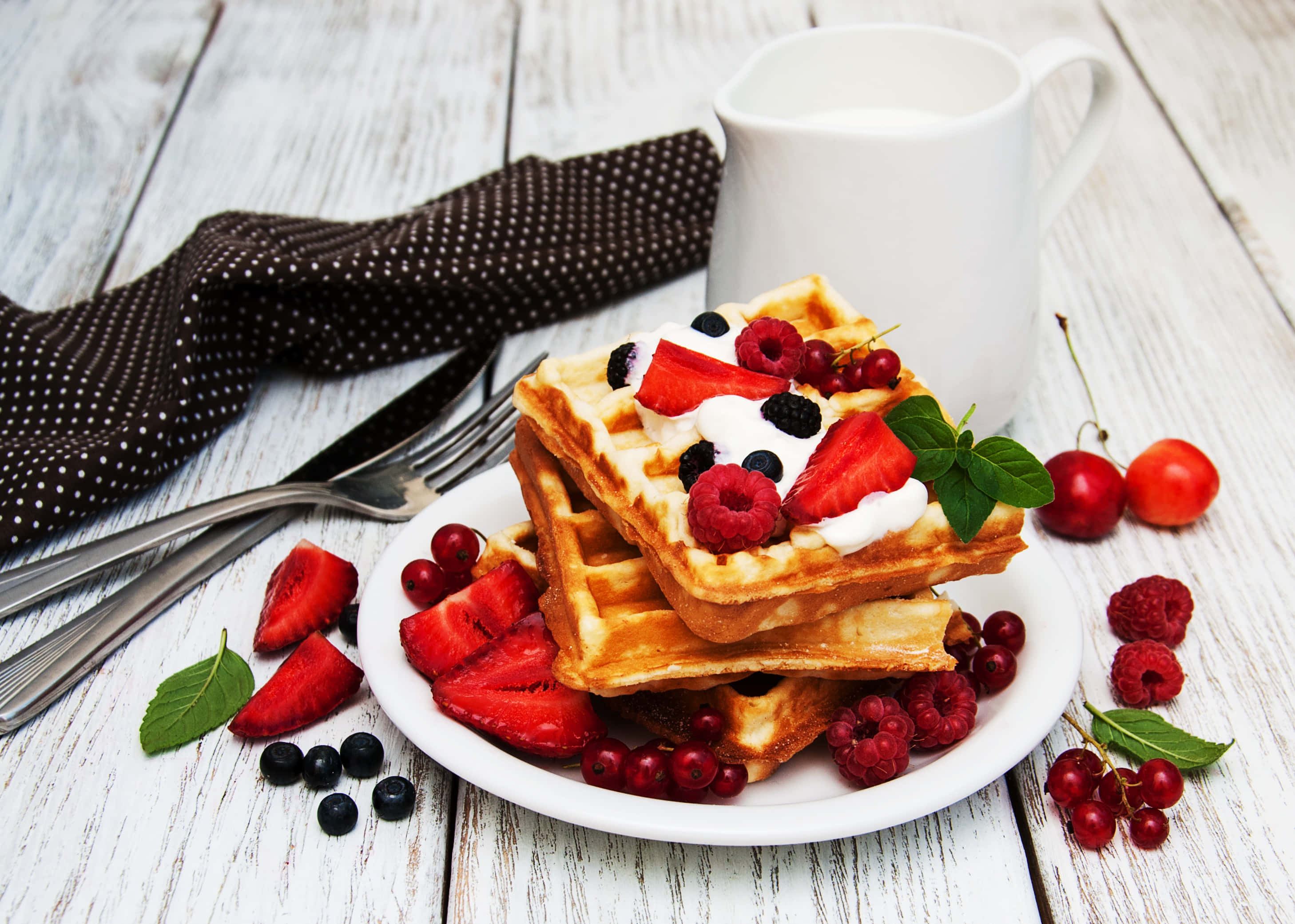 Waffle 桌布 壁紙 — 金黃色鬆餅層層疊起，上面鋪滿新鮮莓果、鮮奶油和薄荷，放在質樸的白色木桌上。