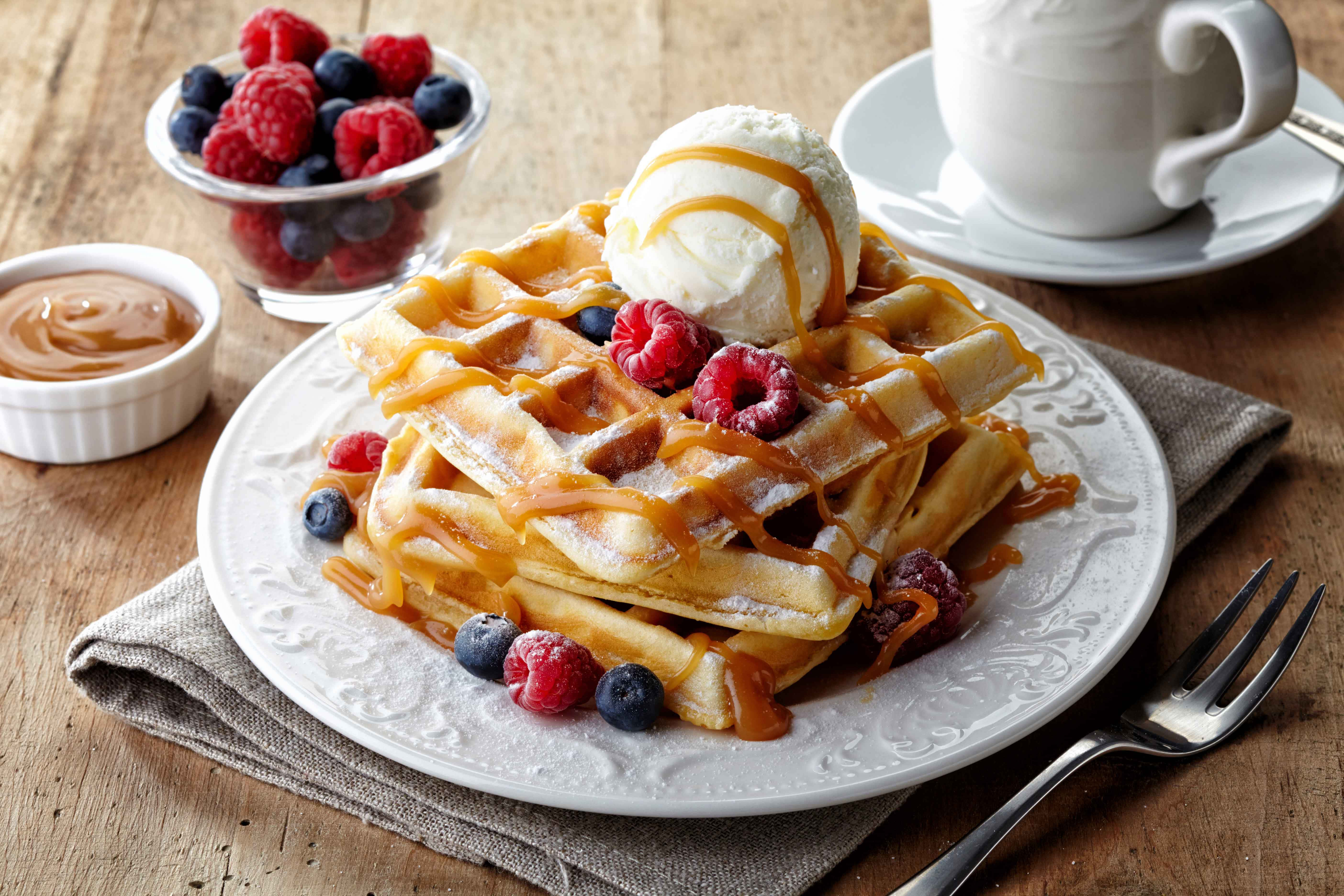 Waffle 桌布 壁紙 — 金黃色鬆餅層層疊起，淋上焦糖醬，搭配冰淇淋和新鮮莓果，放在質樸的木桌上。