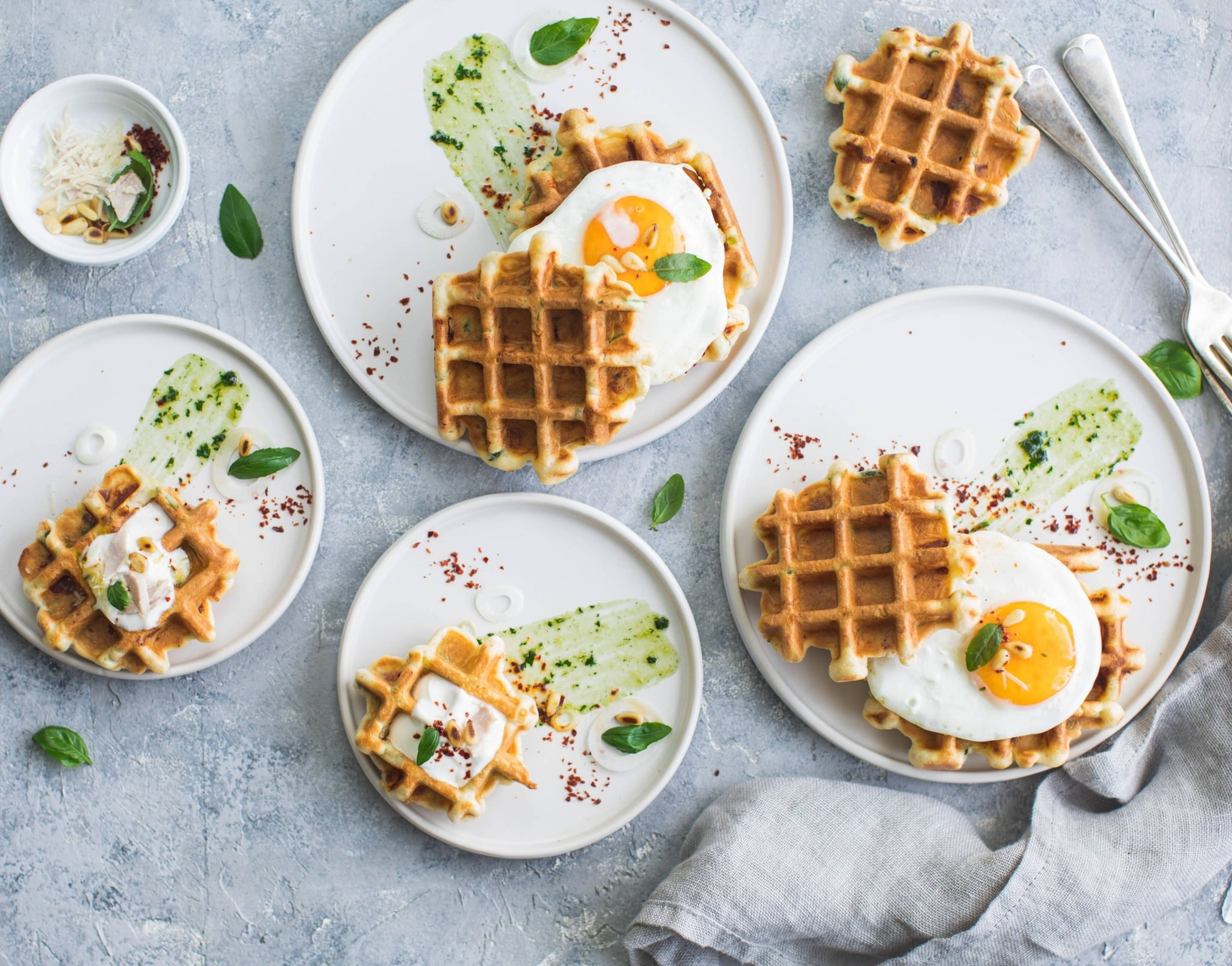 Waffle 桌布 壁紙 — 金黃色鬆餅搭配太陽蛋和新鮮羅勒，放在白色盤子上，置於有紋理的灰色表面。