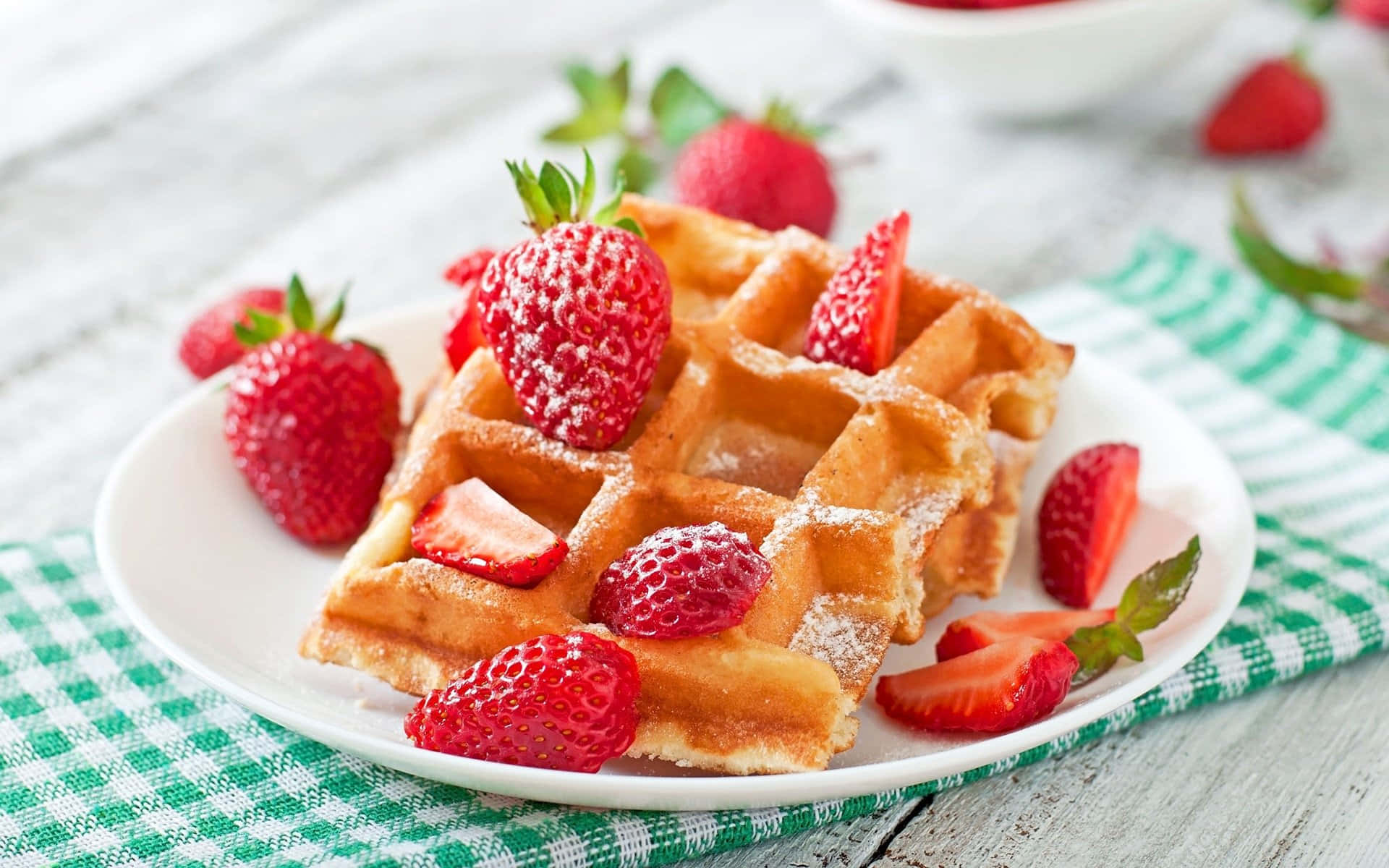 Waffle 桌布 壁紙 — 金黃色鬆餅搭配新鮮草莓和糖粉，放在格子餐巾上。