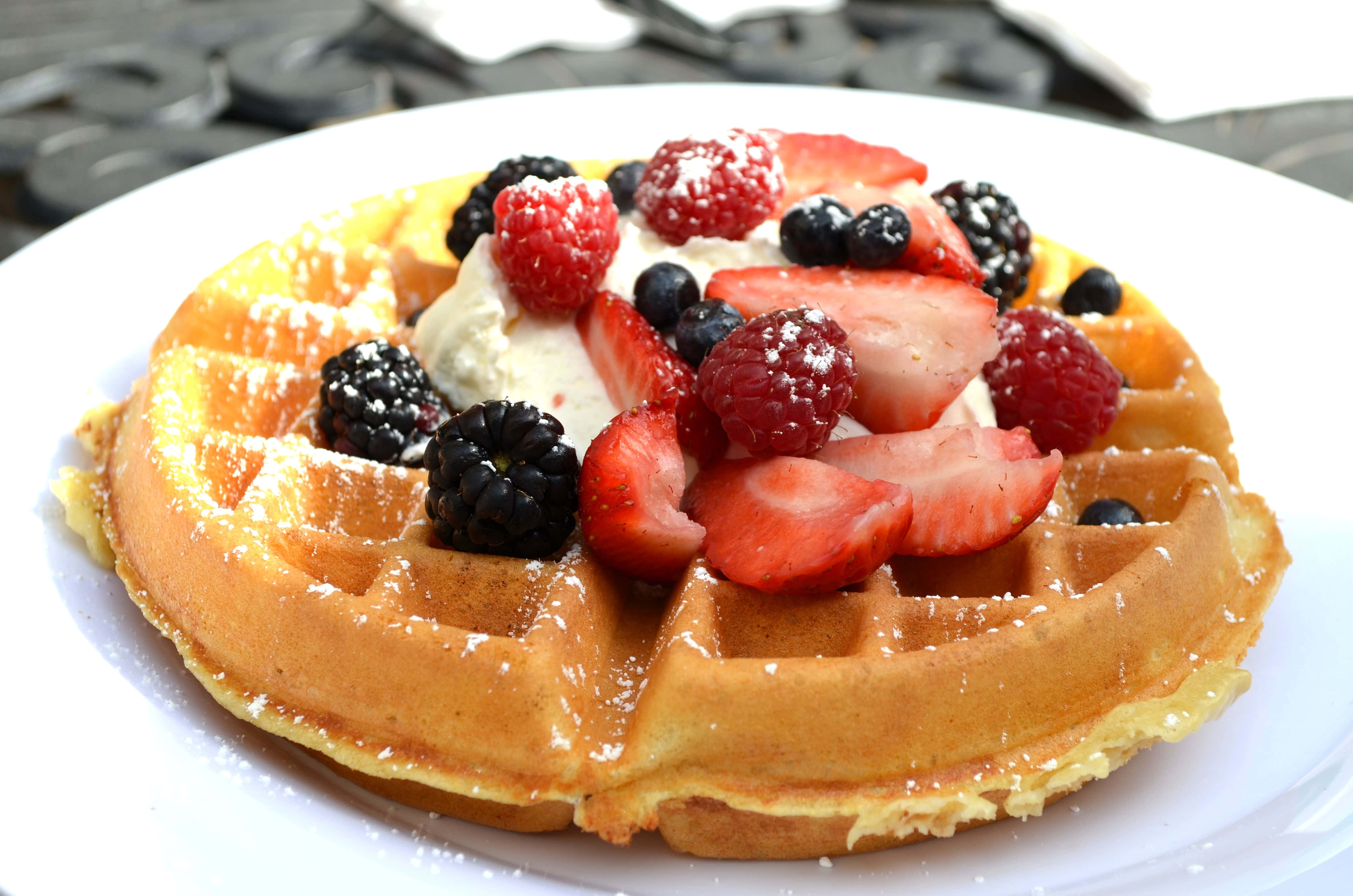 Waffle 桌布 壁紙 — 金黃色鬆餅搭配新鮮莓果、鮮奶油和糖粉，放在白色盤子上。