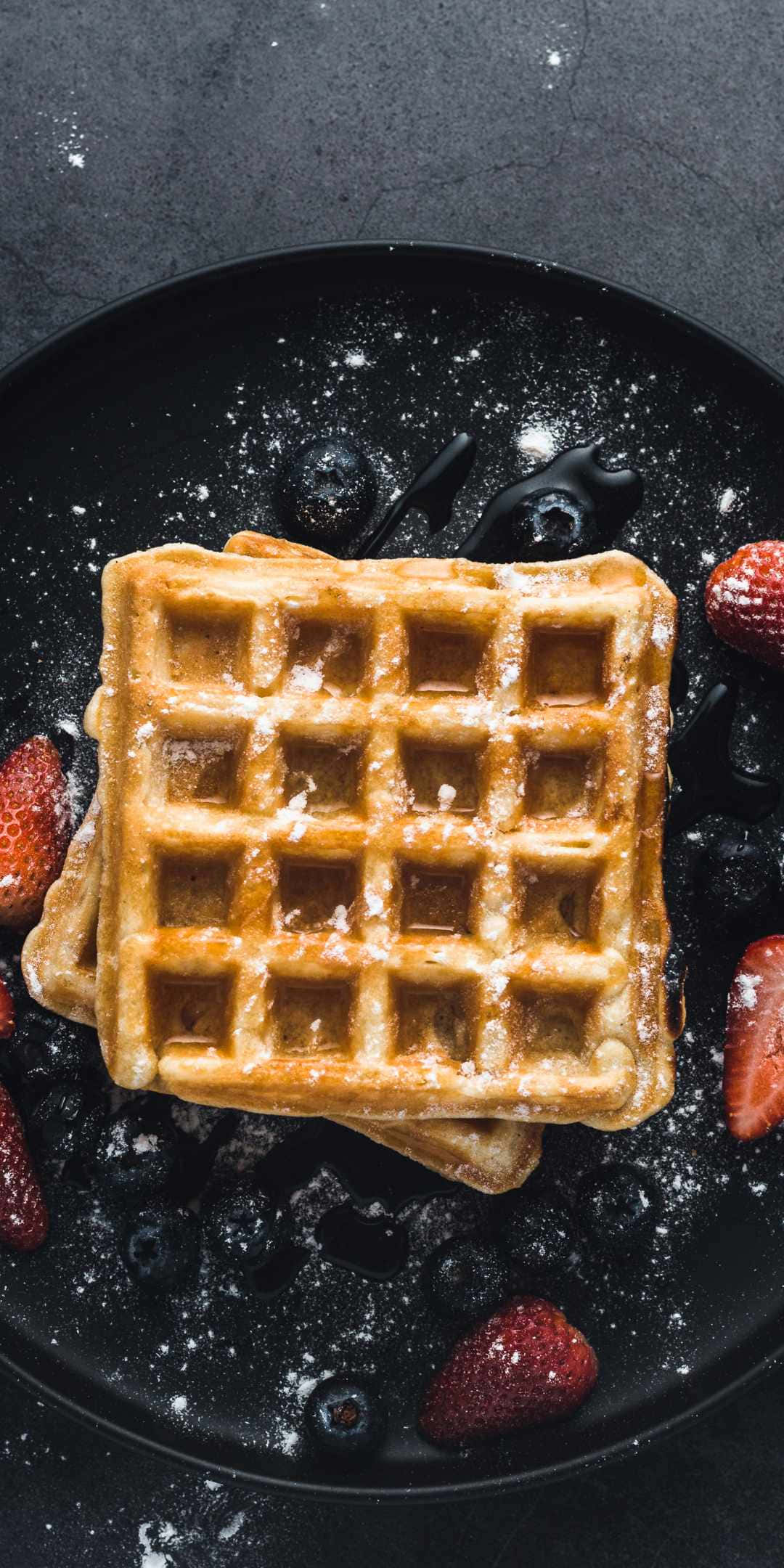 Pastries 桌布 壁紙 — 金黃色鬆餅撒上糖粉，搭配新鮮莓果和糖漿，放在深色盤子上。