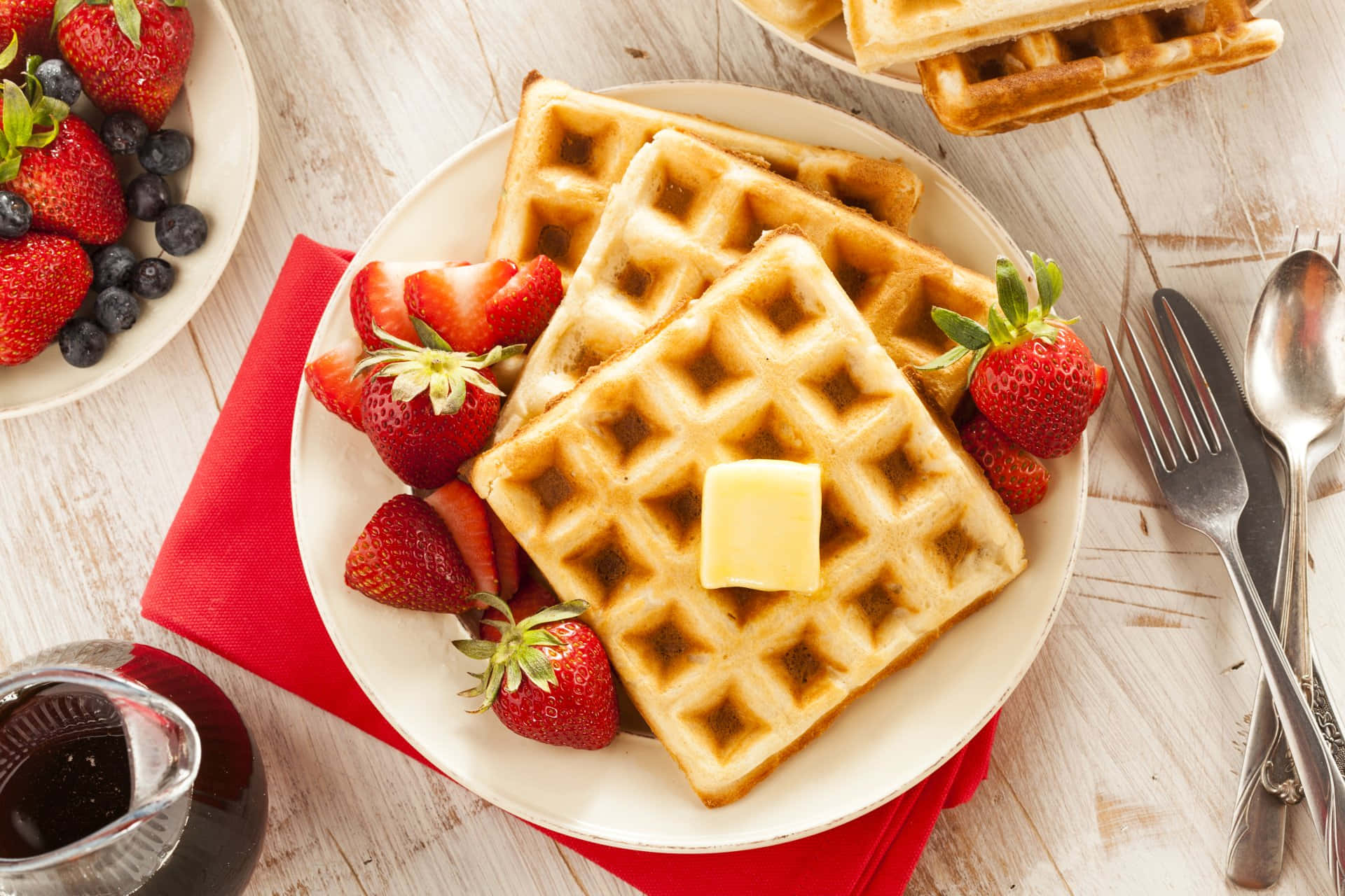 Waffle 桌布 壁紙 — 金黃色鬆餅配上奶油和新鮮草莓，放在白色盤子上，旁邊有一碗莓果和糖漿，置於鄉村風木桌上。