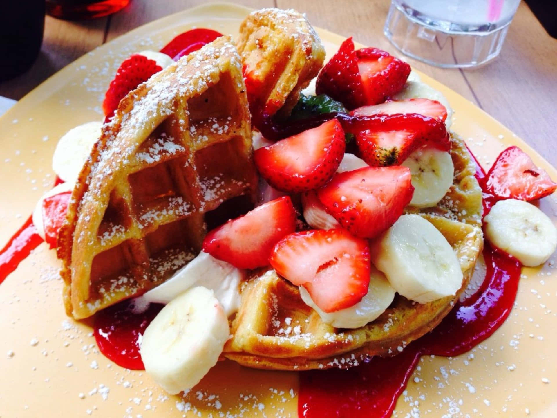 Waffle 桌布 壁紙 — 金黃色鬆餅配上新鮮草莓、香蕉、鮮奶油和草莓糖漿，撒上糖粉。