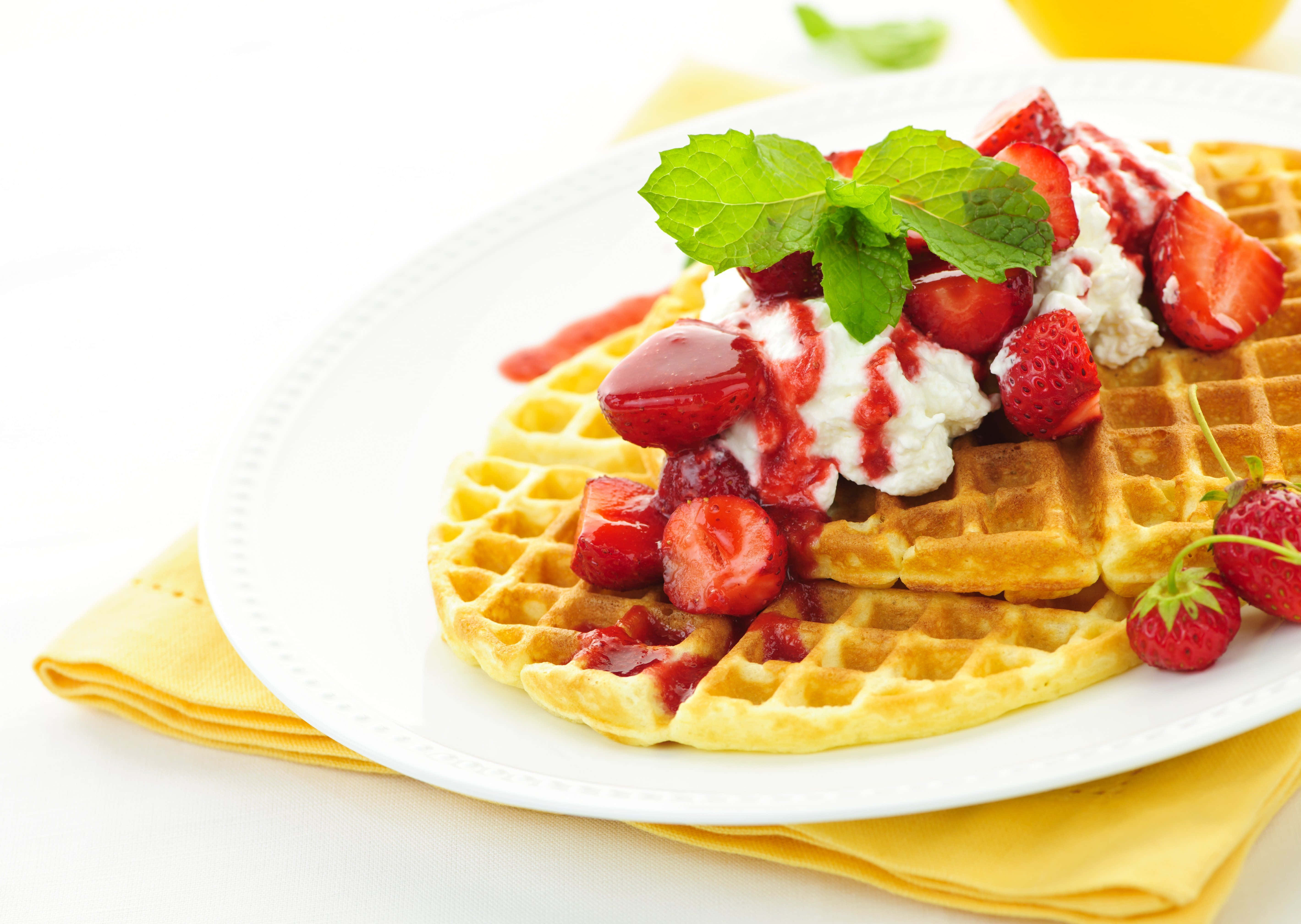 Waffle 桌布 壁紙 — 金黃色鬆餅配上新鮮草莓、鮮奶油和薄荷葉，放在白色盤子上。