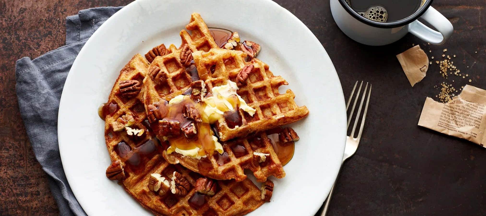 Waffle 桌布 壁紙 — 金黃色鬆餅配上糖漿、奶油和胡桃，放在白色盤子上，旁邊有咖啡杯和叉子，置於深色木桌上。