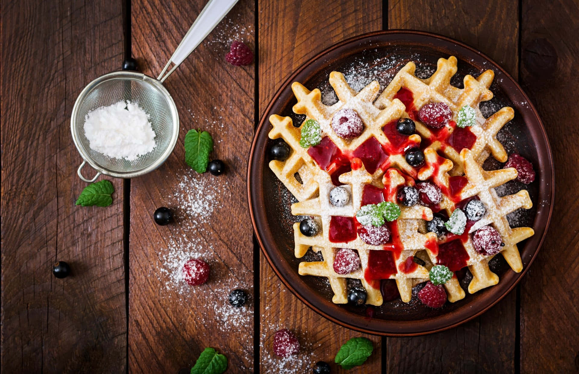Waffle 桌布 壁紙 — 金黃色鬆餅配上莓果、薄荷和糖粉，放在質樸的木桌上，旁邊有一個篩糖器。