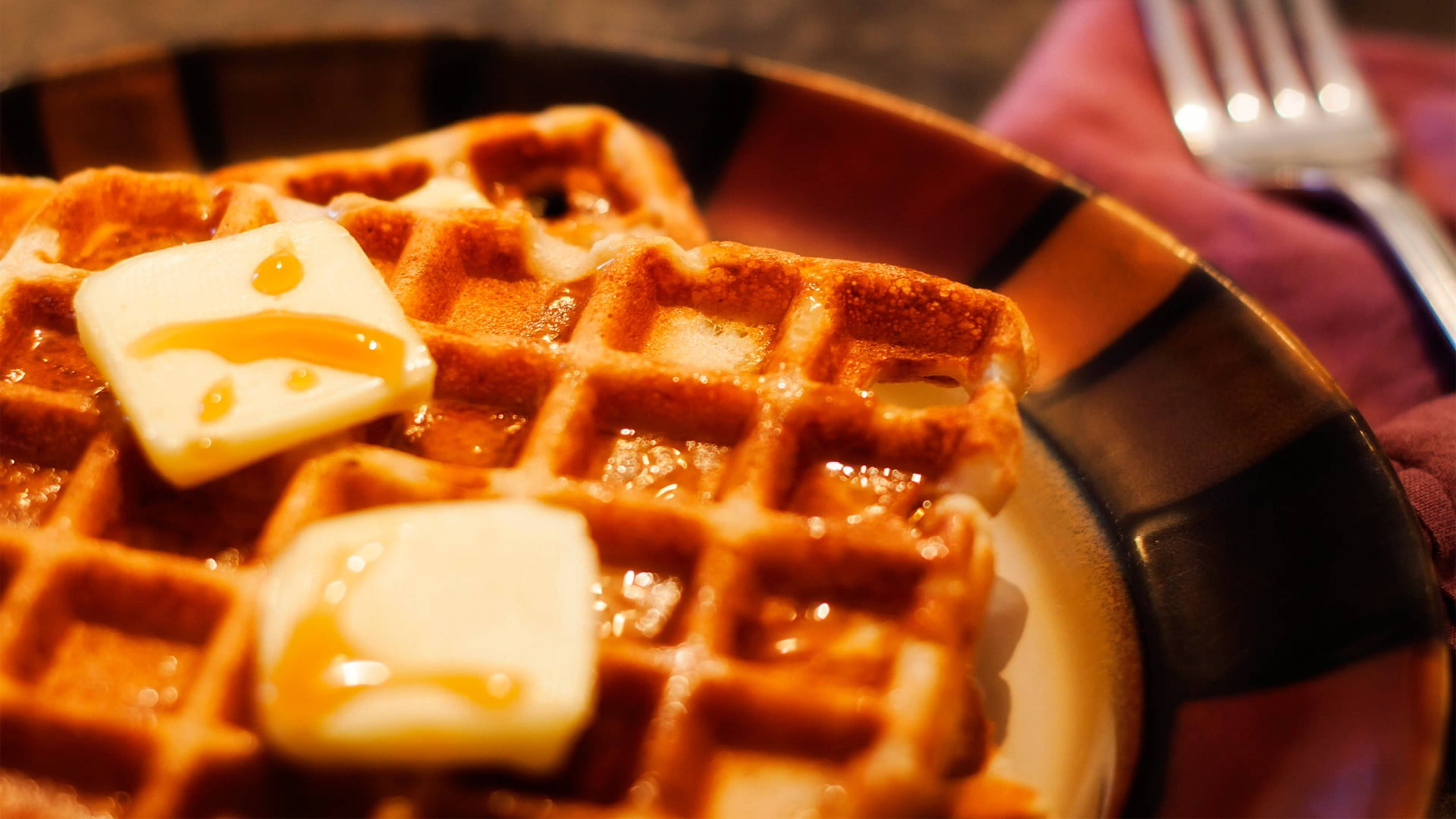 Waffle 桌布 壁紙 — 金黃色鬆餅配上融化奶油和糖漿，在溫暖燈光下於有圖案的盤子上閃閃發光。