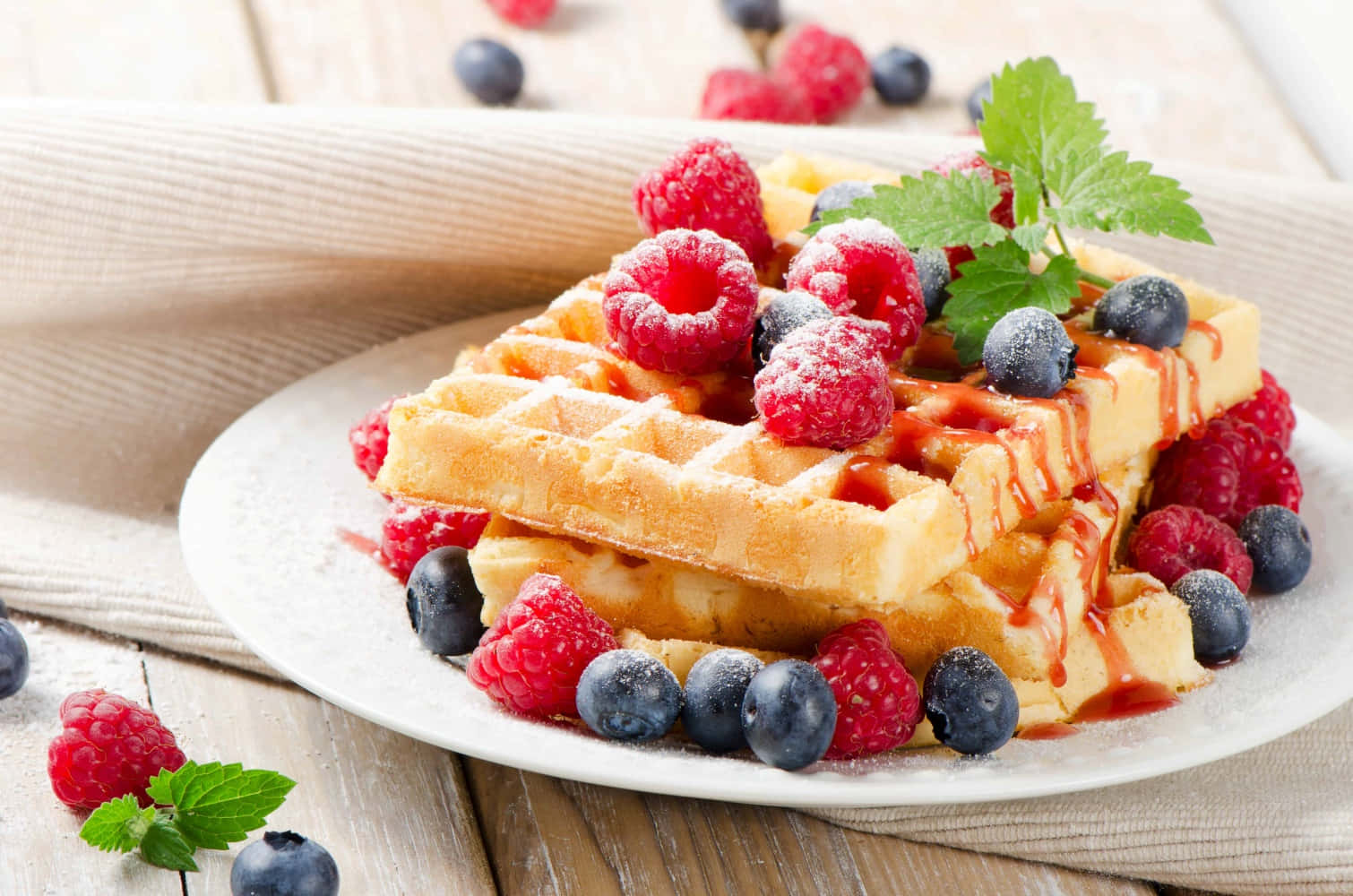 Waffle 桌布 壁紙 — 金黃色鬆餅高高疊起，配上新鮮覆盆子、藍莓和薄荷，淋上糖漿，放在質樸的木桌上。