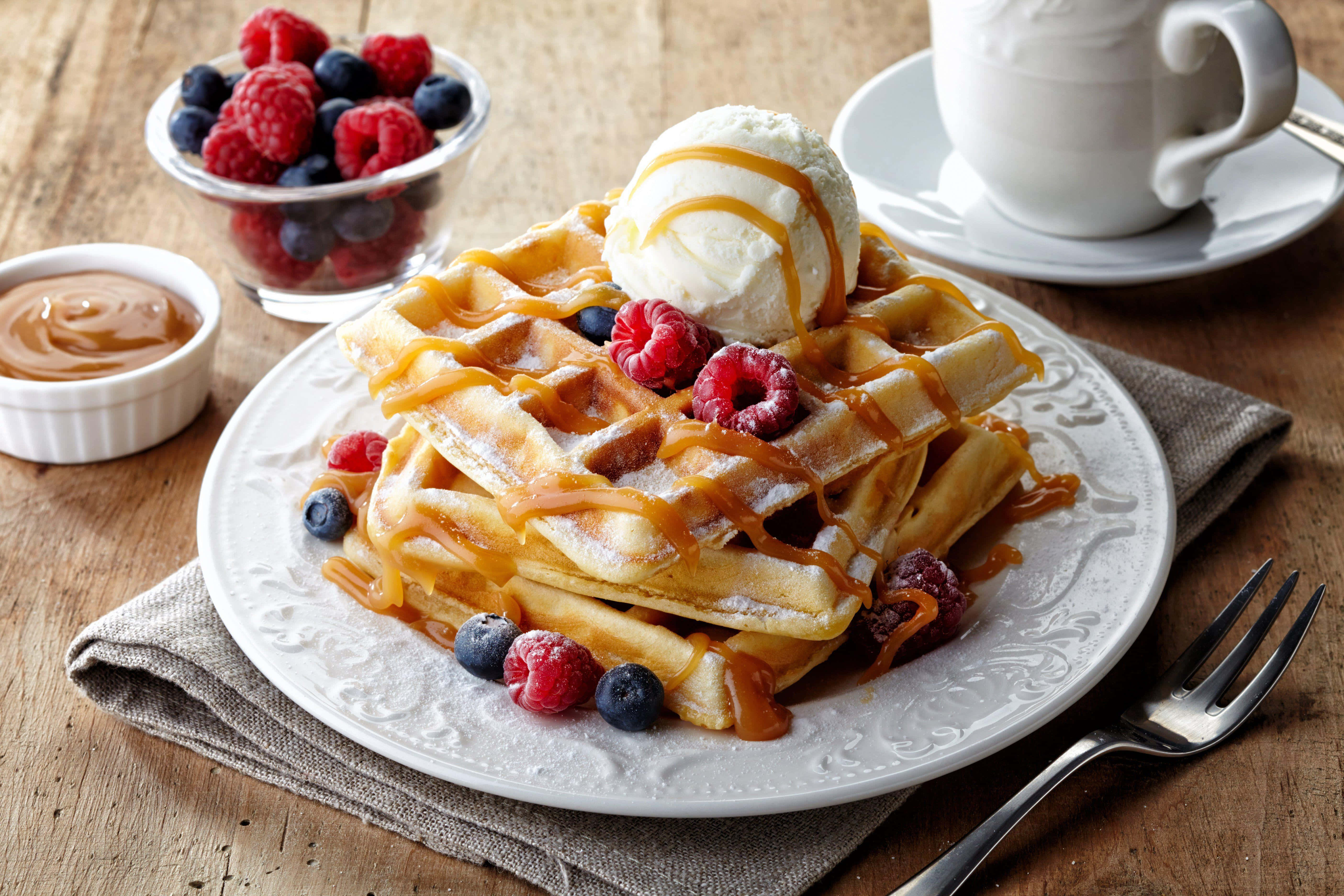Waffle 桌布 壁紙 — 金黃色鬆餅高高疊起，配上焦糖醬、莓果和香草冰淇淋，放在質樸的木桌上。