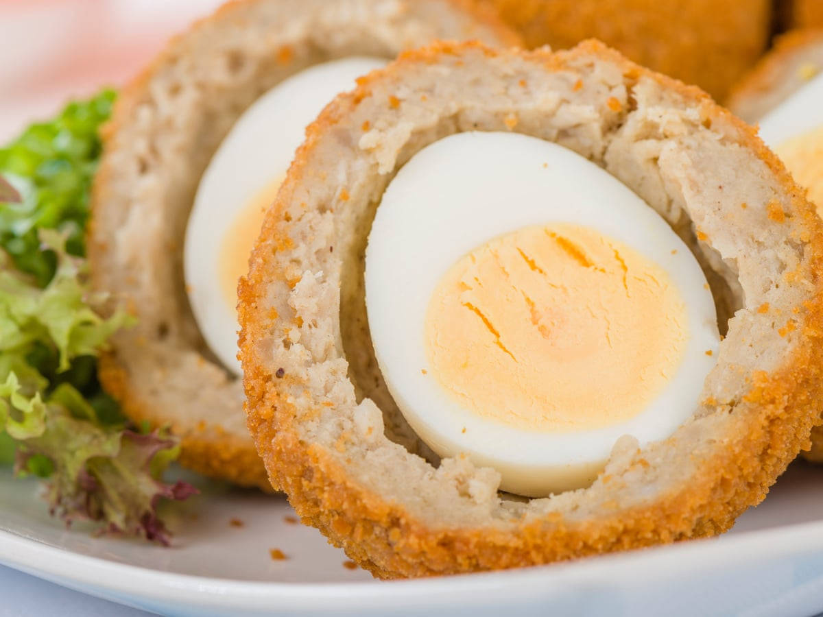 Egg 桌布 壁紙 — 金黃色麵包糠蘇格蘭蛋切開的特寫，露出 creamy 蛋黃和蛋白中心，搭配新鮮生菜。