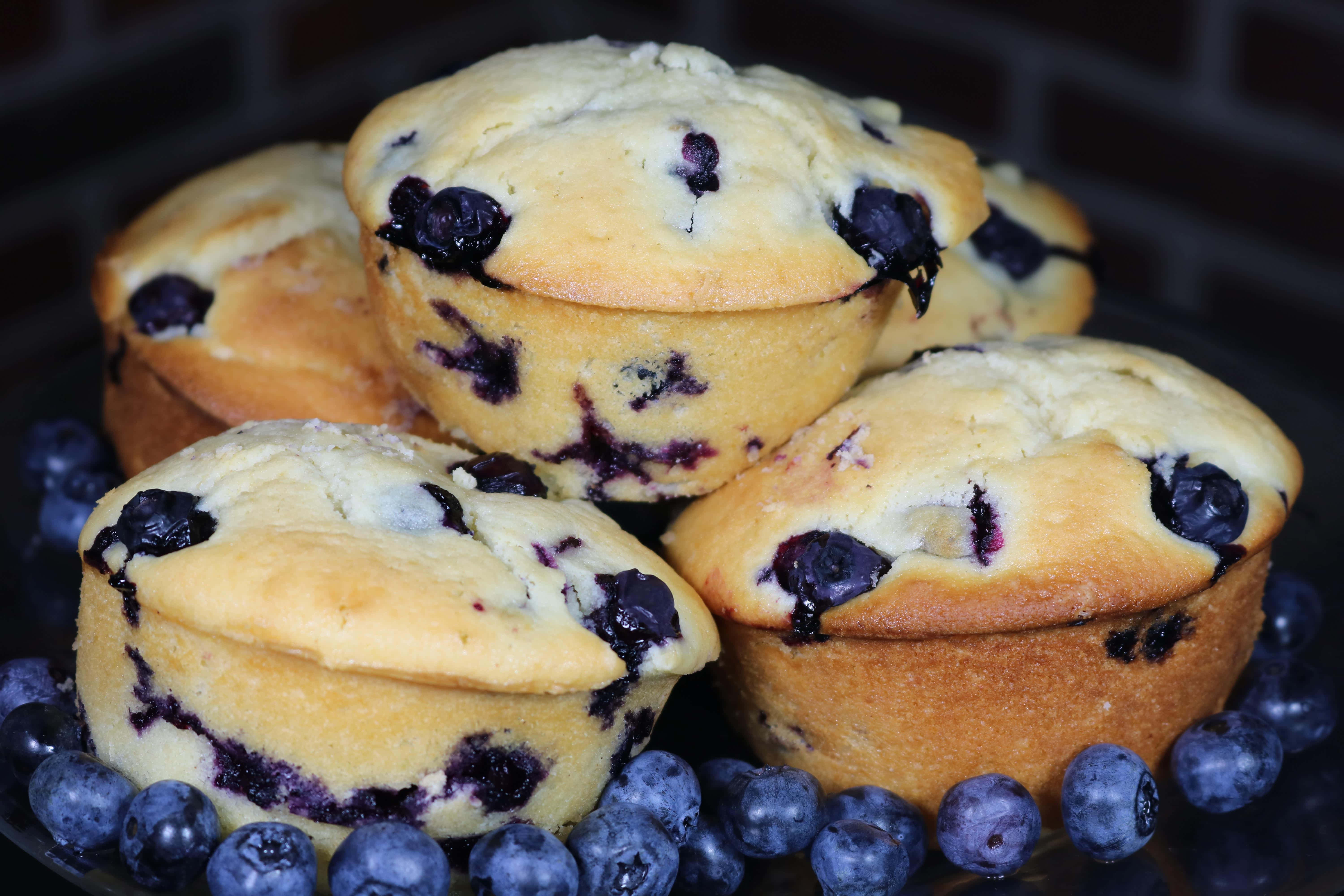 Blueberry Muffins 桌布 壁紙 — 金黃藍莓馬芬高高堆疊，新鮮莓果在柔和光線下閃閃發光。