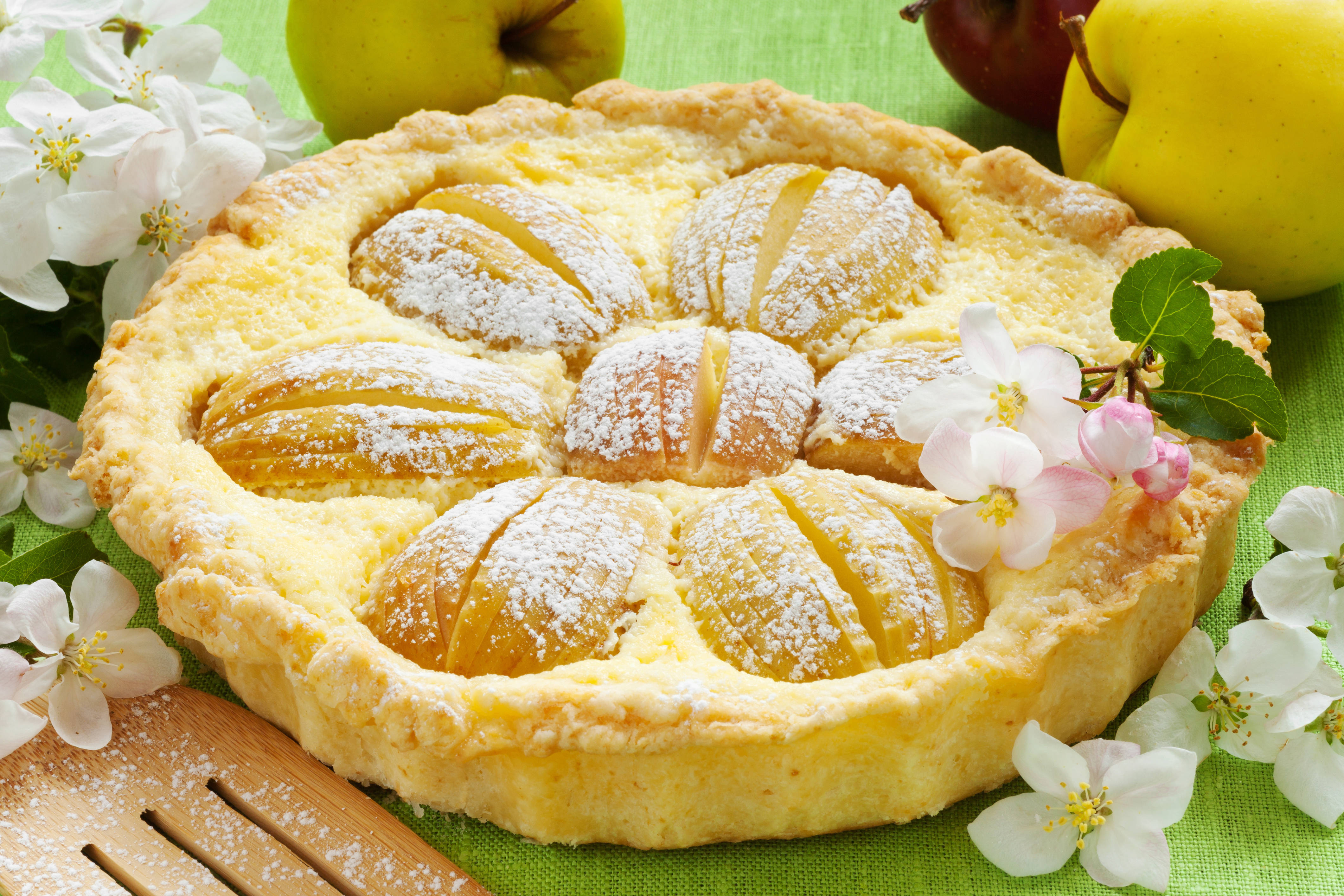 Pie 桌布 壁紙 — 金黃蘋果塔撒上糖粉，周圍放上新鮮蘋果和精緻的白色花朵，置於綠色布上。