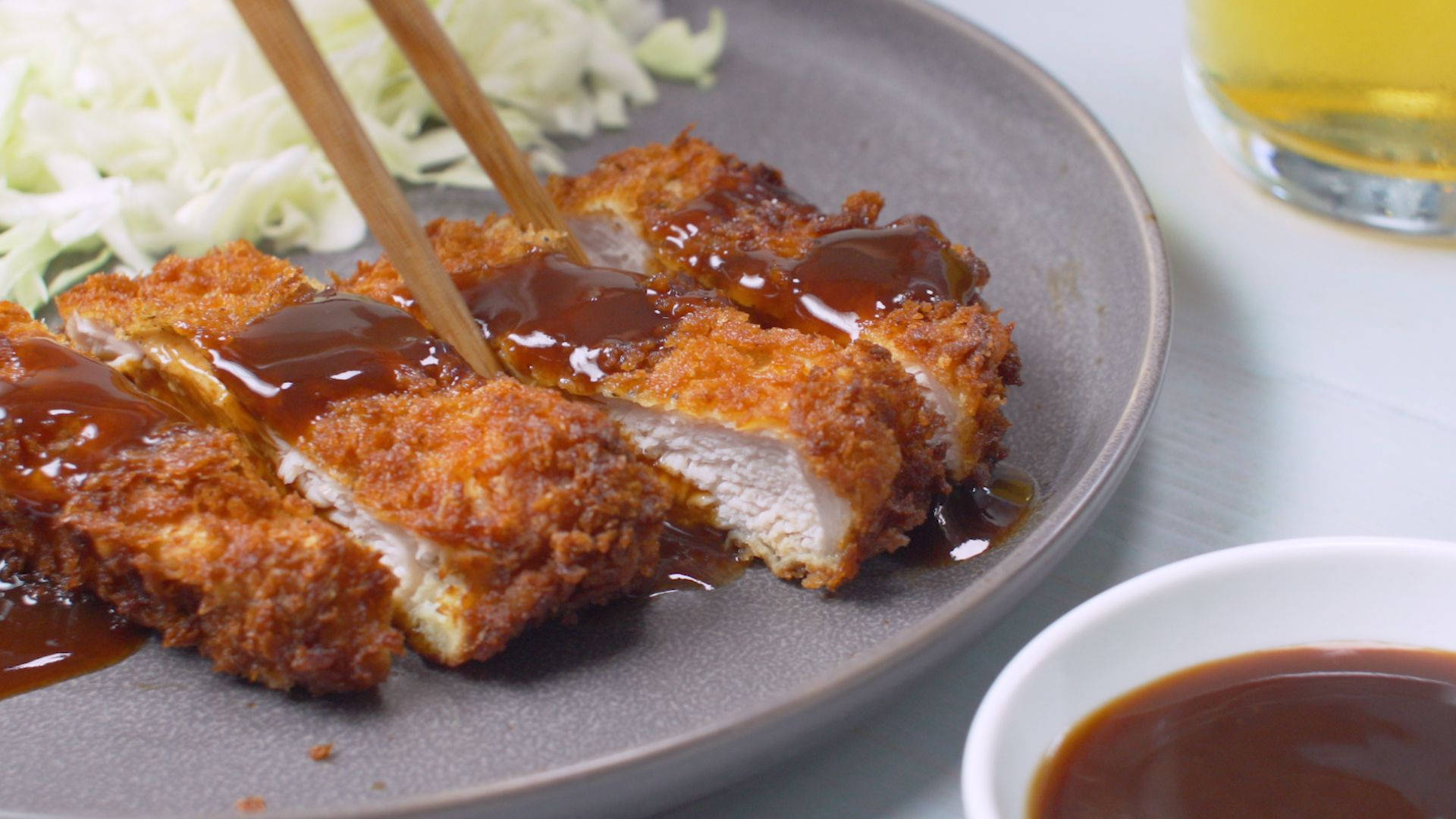 Food Photography 桌布 壁紙 — 金黃酥脆的吉列豬排切片，淋上光澤醬汁，放在灰色盤子上，搭配高麗菜絲和蘸醬。
