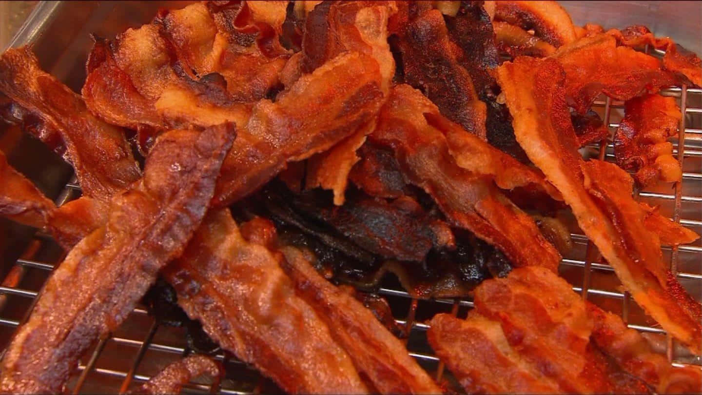 bacon 桌布 壁紙 — 金黃酥脆的培根條在金屬冷卻架上滋滋作響，帶有閃亮的油脂和焦黑的邊緣。