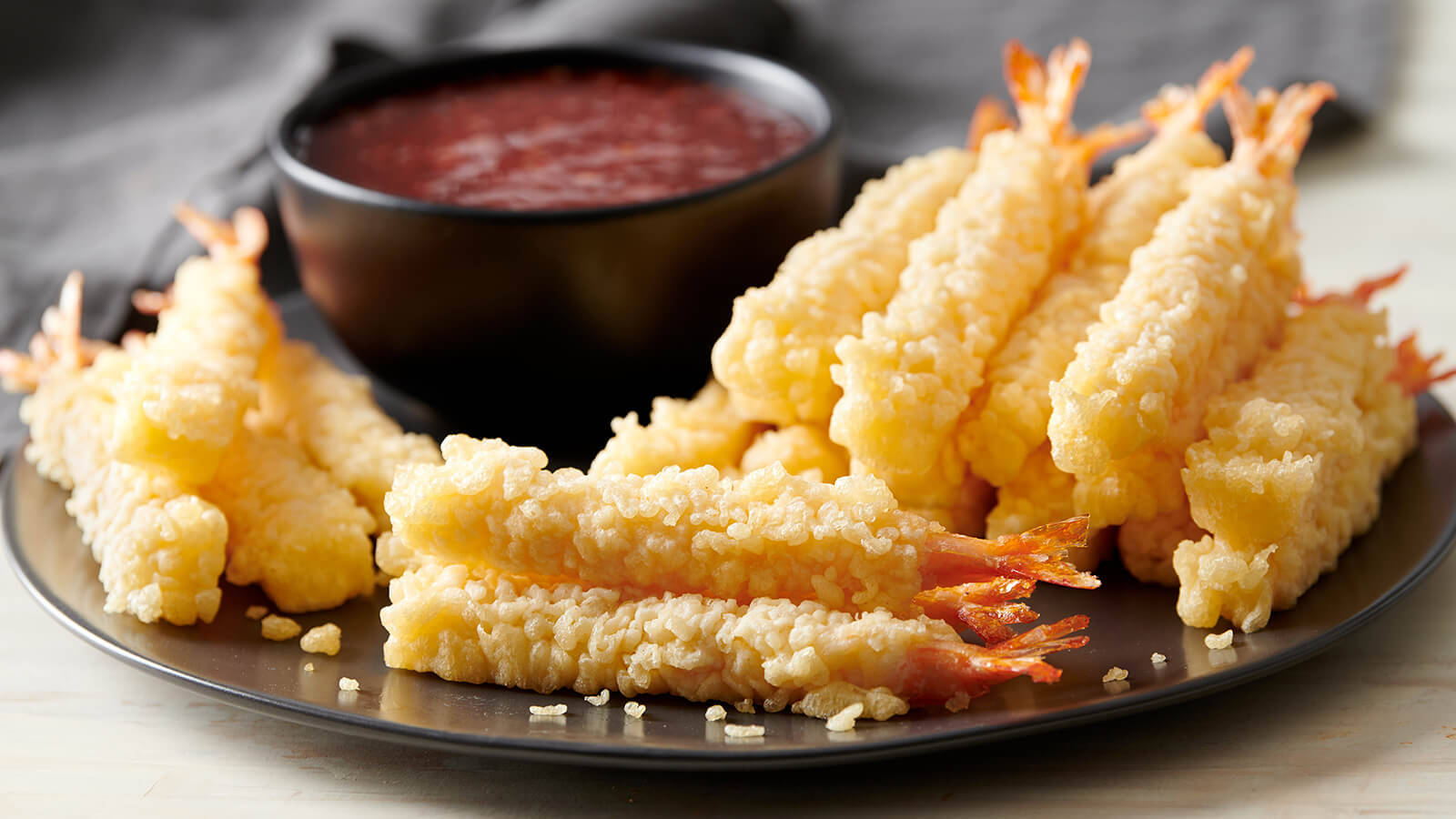 shrimp 桌布 壁紙 — 金黃酥脆的天婦羅蝦堆在深色盤子上，旁邊放著一碗紅色蘸醬。