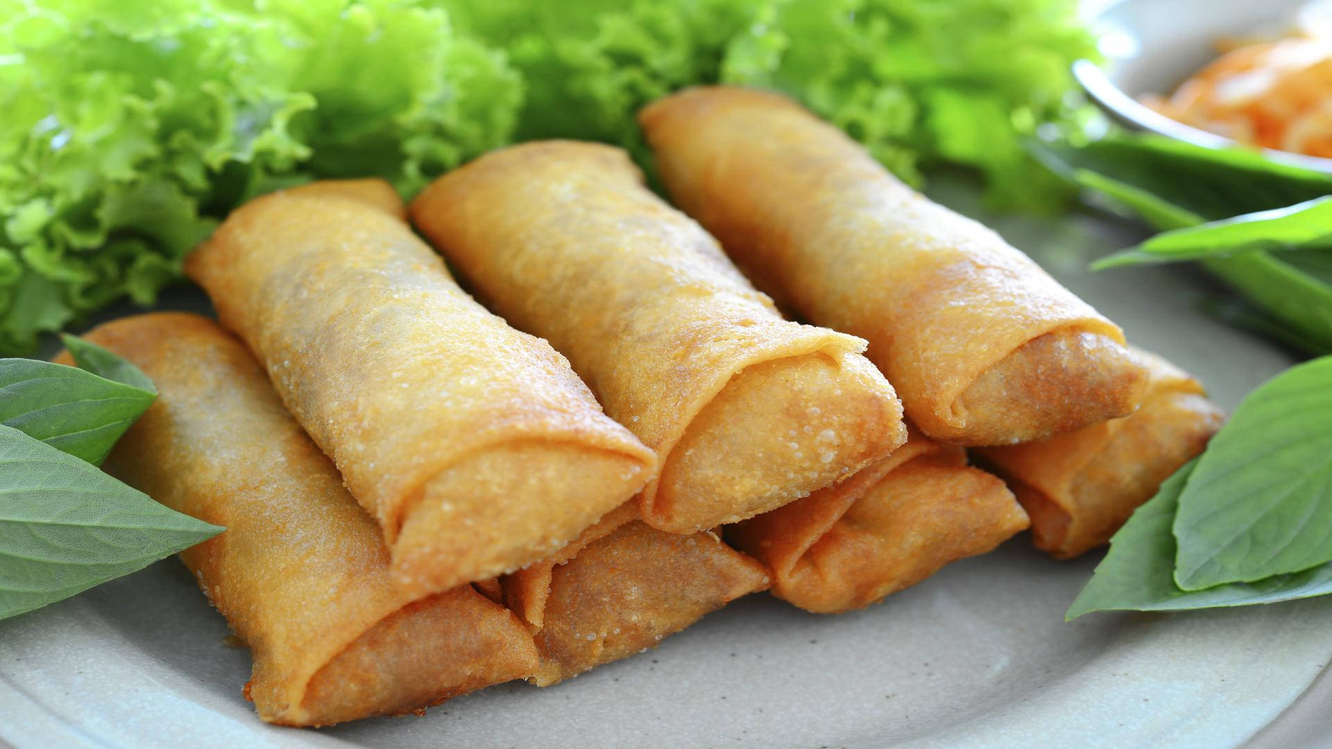 Egg 桌布 壁紙 — 金黃酥脆的春捲堆放在盤子上，搭配新鮮的綠色生菜和羅勒葉。