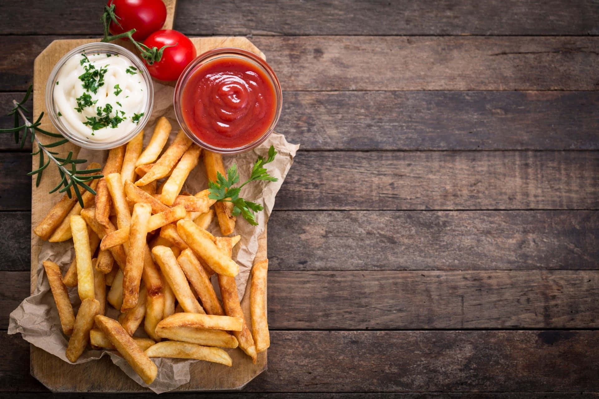 fast food 桌布 壁紙 — 金黃酥脆的炸薯條放在木板上，配上番茄醬和酸奶油，並以新鮮香草點綴。