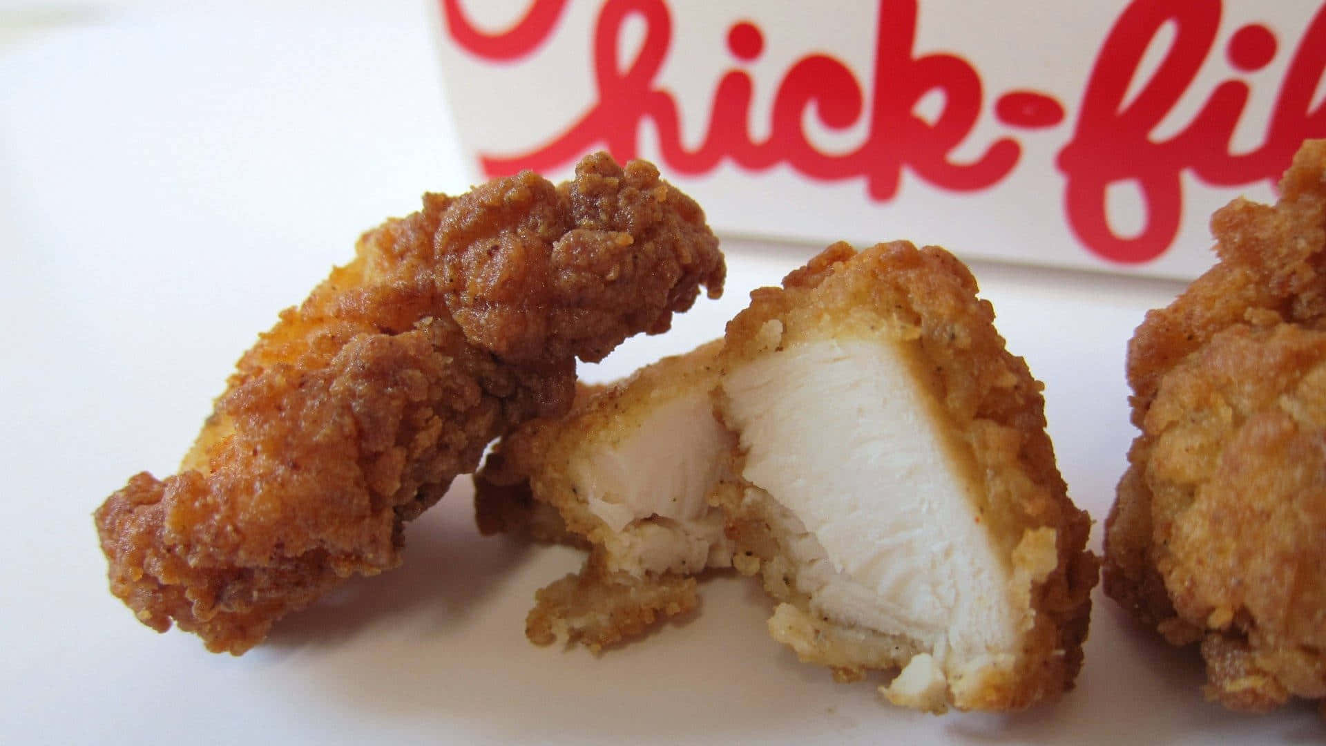 Chick Fil A 桌布 壁紙 — 金黃酥脆的炸雞塊，露出多汁的白肉，放在白色盤子上，旁邊有Chick-fil-A標誌。