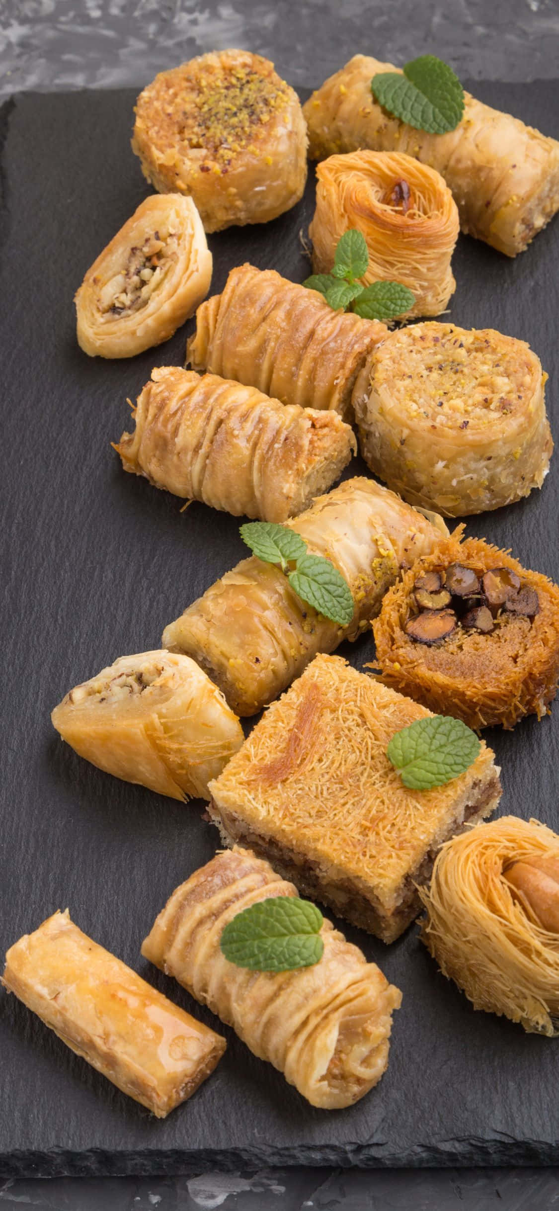 Pastry 桌布 壁紙 — 金黃酥脆的糕點和果仁蜜餅卷，飾以薄荷葉，擺放在深色石板托盤上。