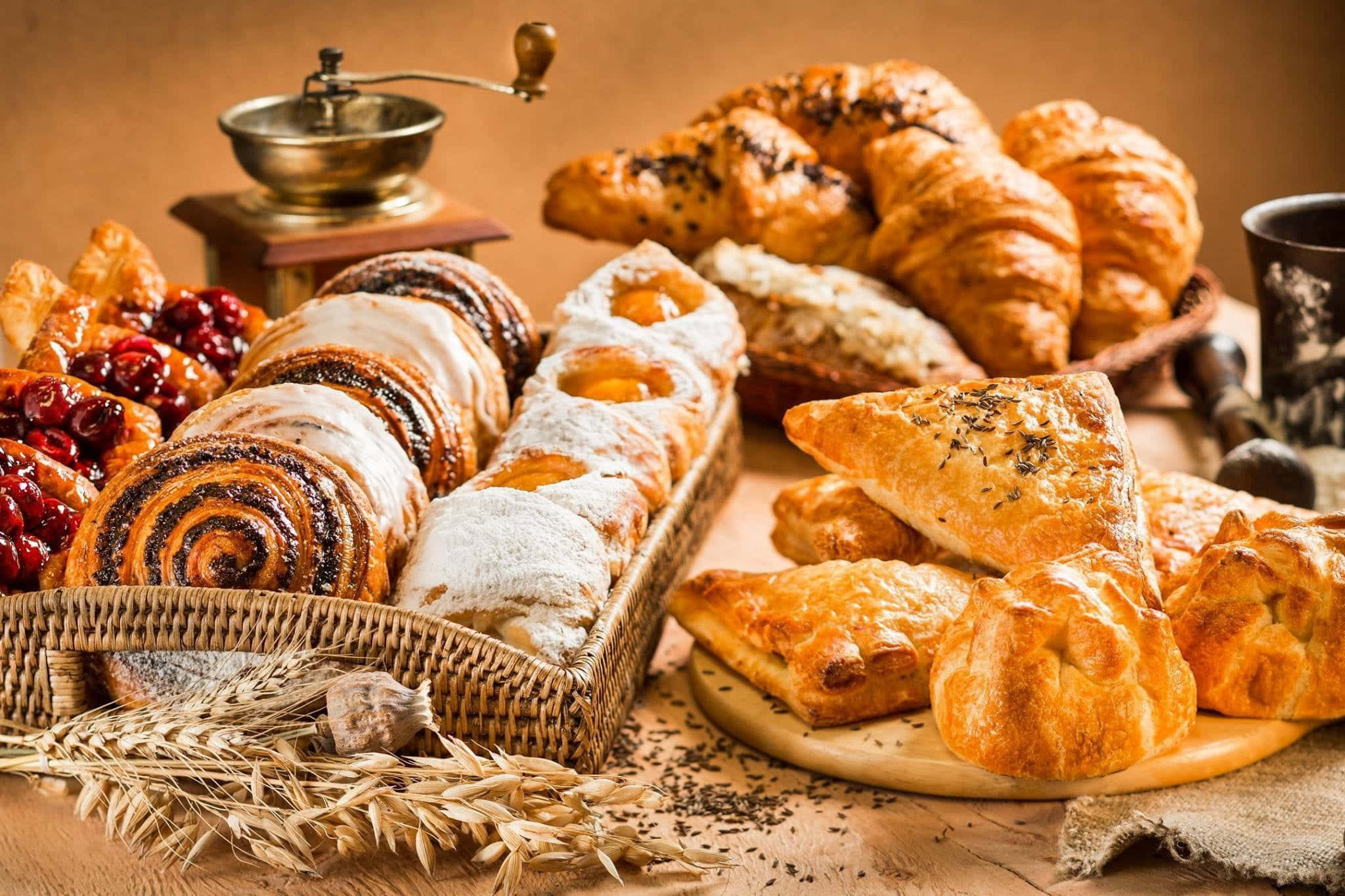 Pastries 桌布 壁紙 — 金黃酥脆的糕點和肉桂卷，搭配麥穗和復古咖啡研磨機，誘人地擺放在質樸的木質表面上。