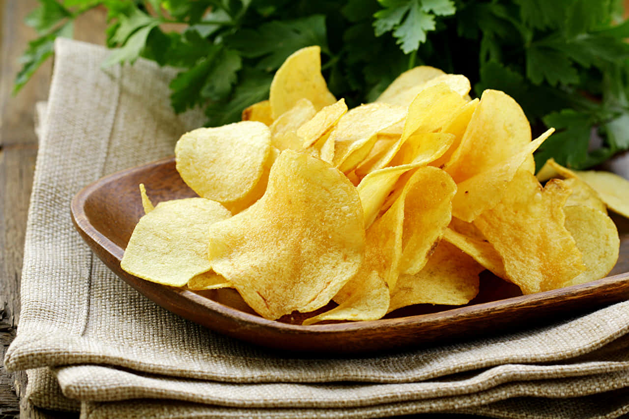 Snacks 桌布 壁紙 — 金黃酥脆的薯片堆在木碗裡，放在米色布上，背景有新鮮的綠色歐芹。