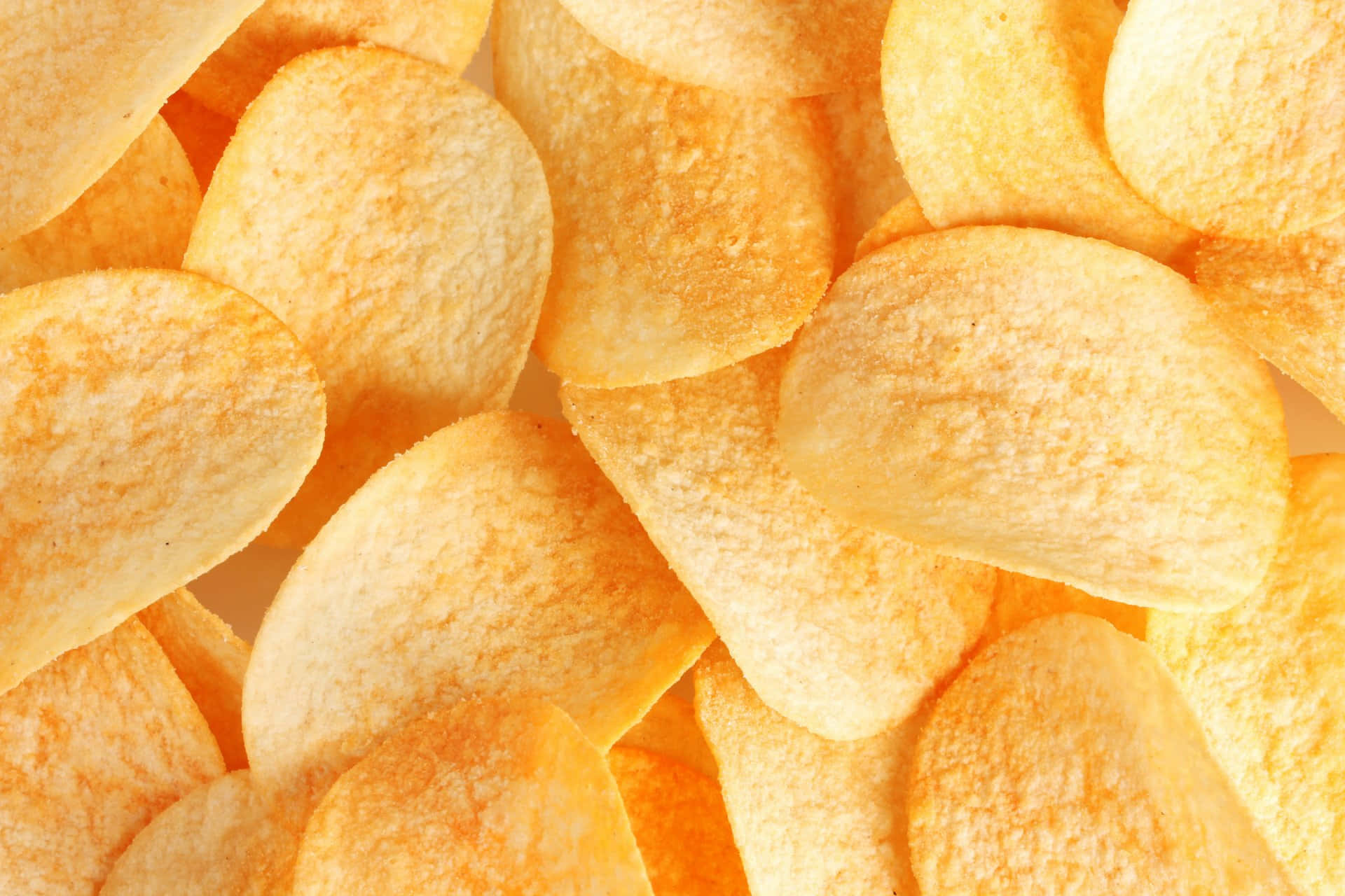 Snacks 桌布 壁紙 — 金黃酥脆的薯片堆疊在一起，特寫鏡頭，表面有紋理，光線溫暖。