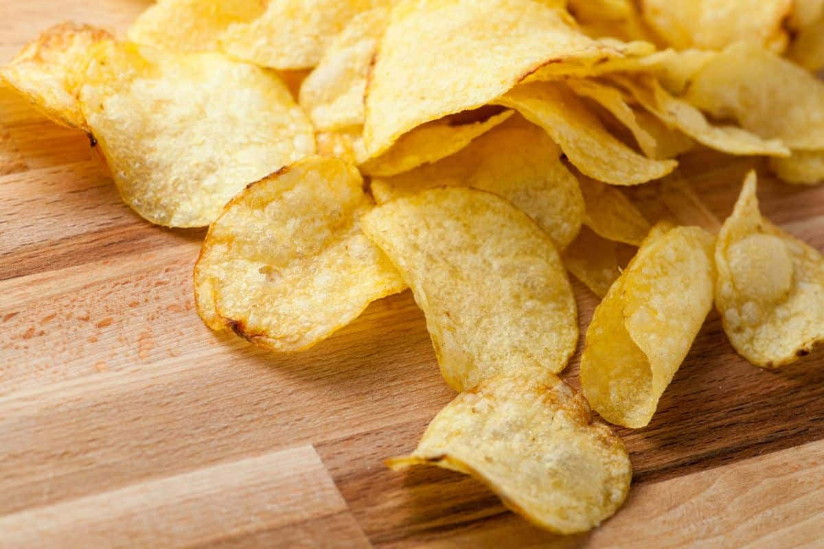 Snacks 桌布 壁紙 — 金黃酥脆的薯片散落在溫暖的木質表面上，木紋清晰可見。