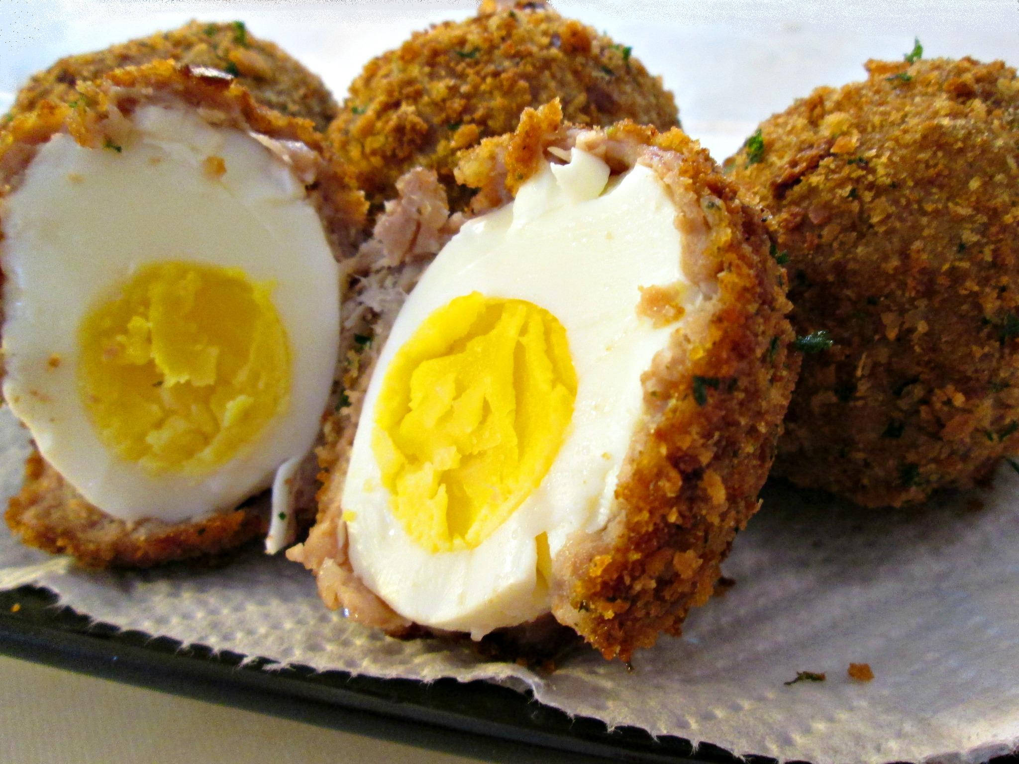 Egg 桌布 壁紙 — 金黃酥脆的蘇格蘭蛋切開，露出奶油般的白色和鮮黃色的蛋黃，放在紙巾上。