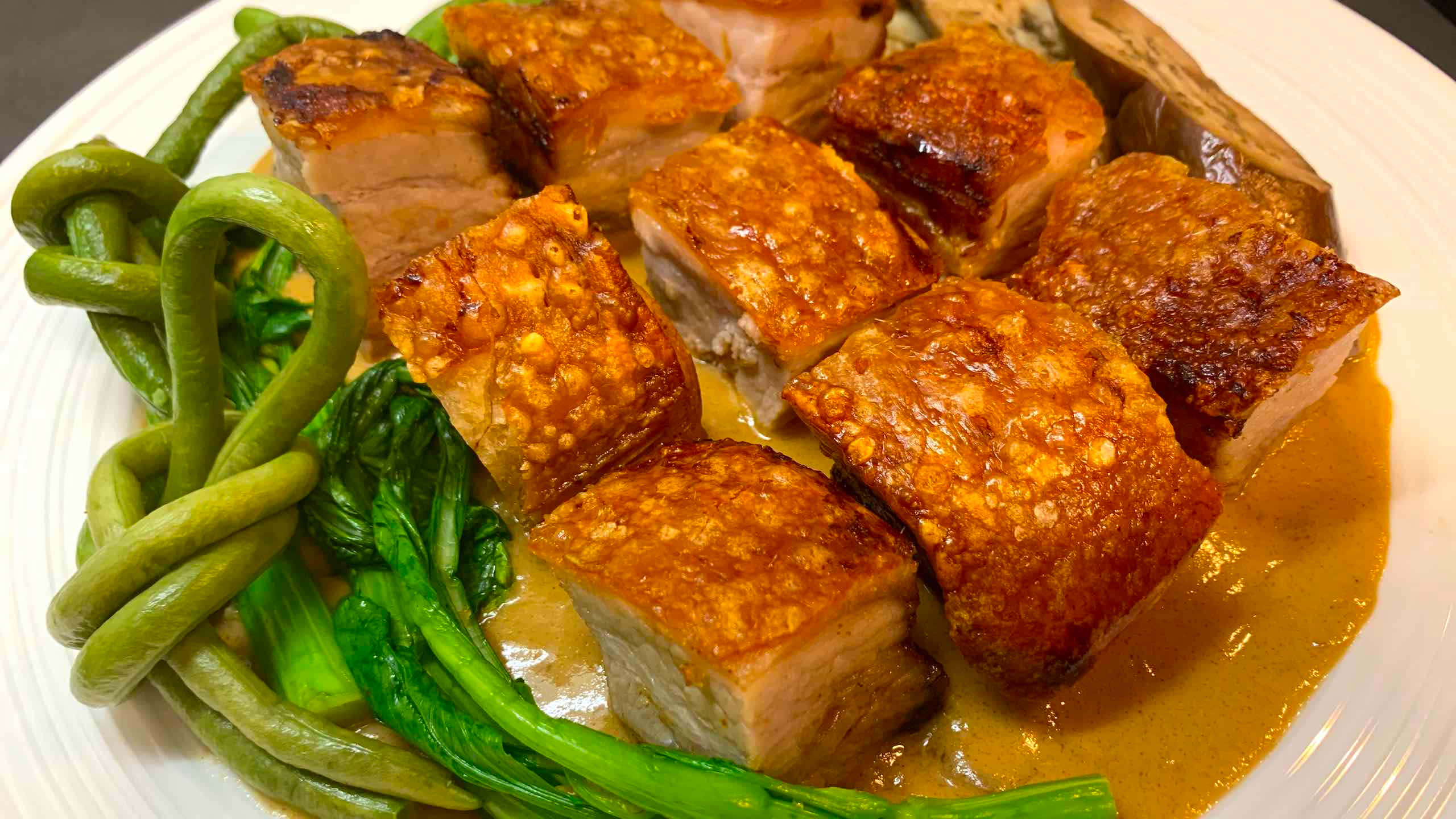 meat 桌布 壁紙 — 金黃酥脆的豬五花肉塊在濃郁的棕色醬汁中閃閃發光，旁邊是鮮綠色的青江菜和四季豆，盛在白色盤子上。
