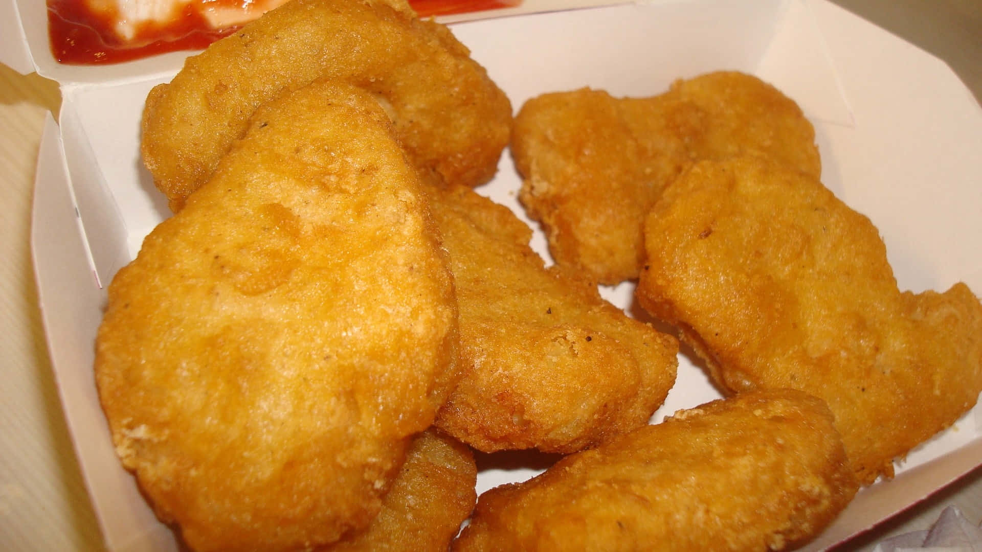 Chicken Nuggets 桌布 壁紙 — 金黃酥脆的雞塊堆疊在白色外帶盒中，搭配紅色沾醬。