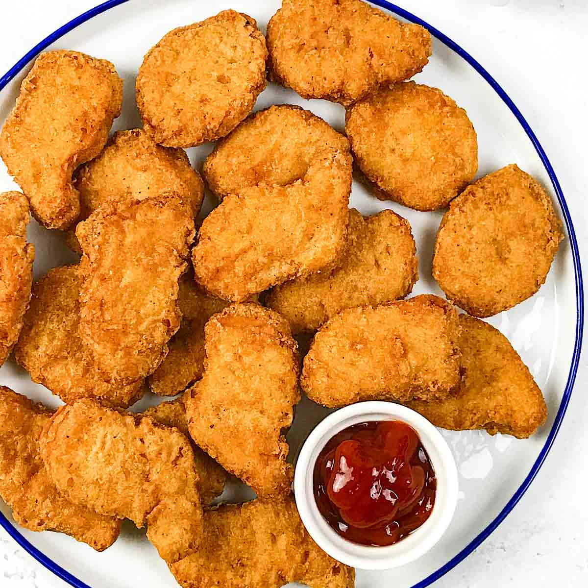 Chicken Nuggets 桌布 壁紙 — 金黃酥脆的雞塊高高堆在帶藍邊的白色盤子上，旁邊有番茄醬。
