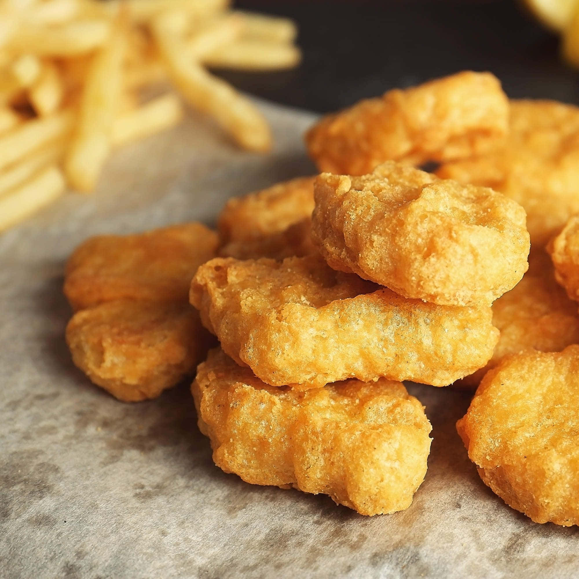 Chicken Nuggets 桌布 壁紙 — 金黃酥脆的雞塊高高堆在烘焙紙上，背景是模糊的薯條。