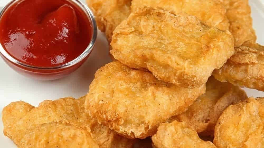 Chicken Nuggets 桌布 壁紙 — 金黃酥脆的雞塊高高堆起，旁邊放著一小碗鮮紅色的番茄醬，置於白色盤子上。