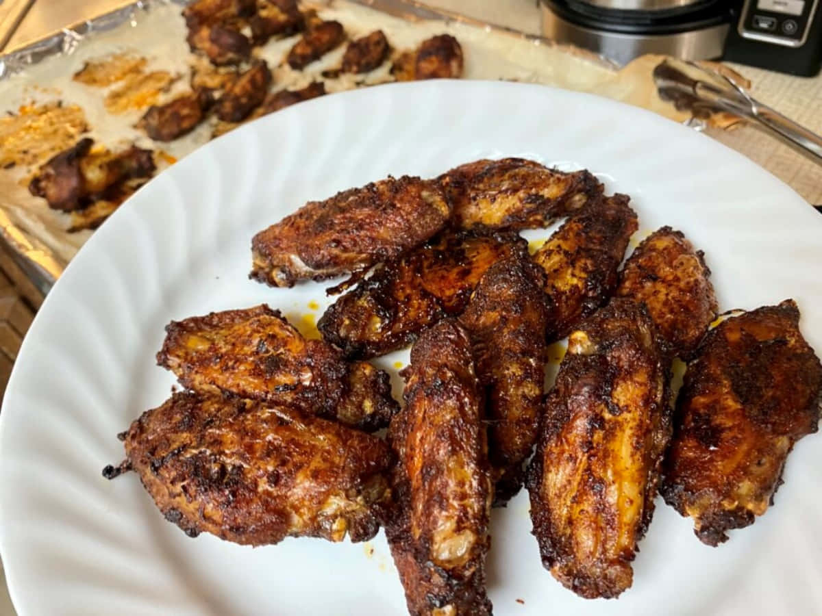 Blackened Chicken 桌布 壁紙 — 金黃酥脆的雞翅高高堆在白色盤子上，後面有更多雞翅放在鋪了鋁箔紙的烤盤上。