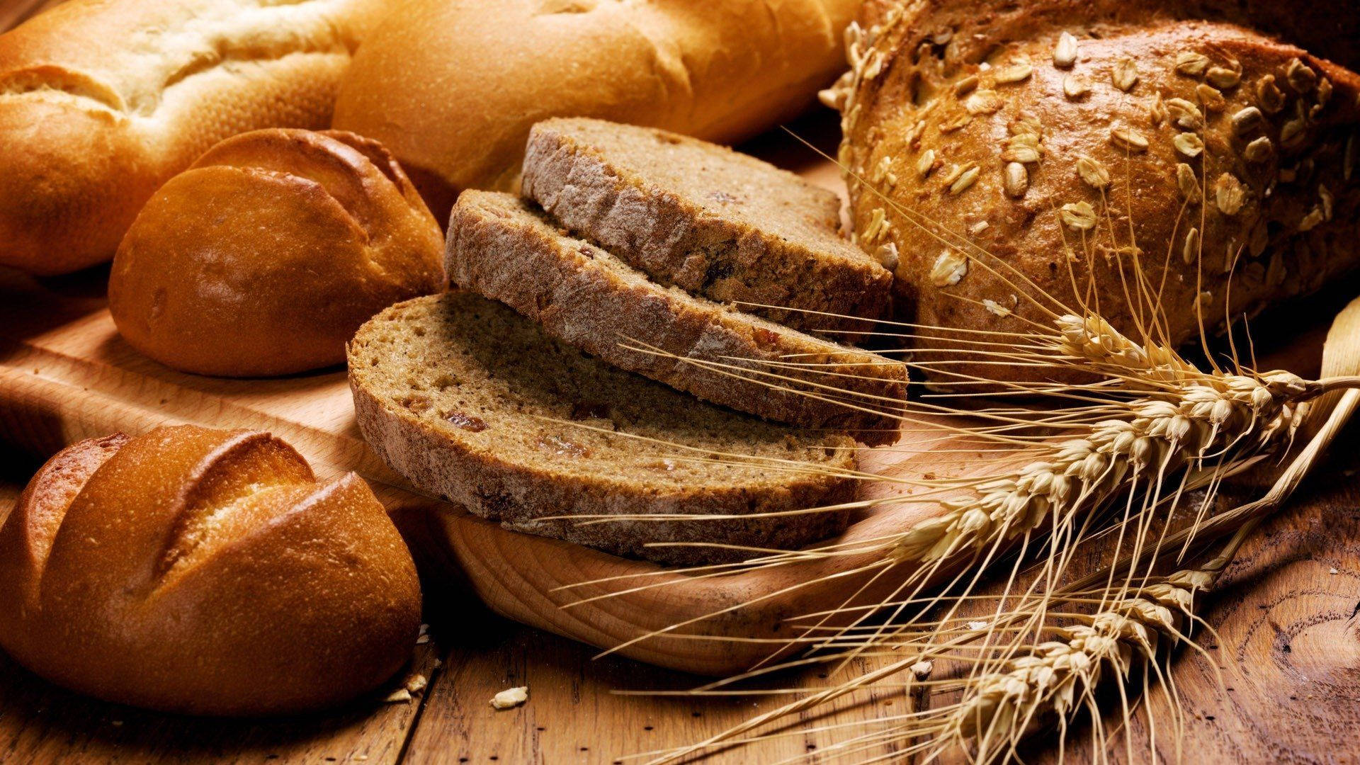 Bread 桌布 壁紙 — 金黃酥脆的麵包和切片鄉村麵包，搭配小麥莖，擺放在溫暖的木質表面上。