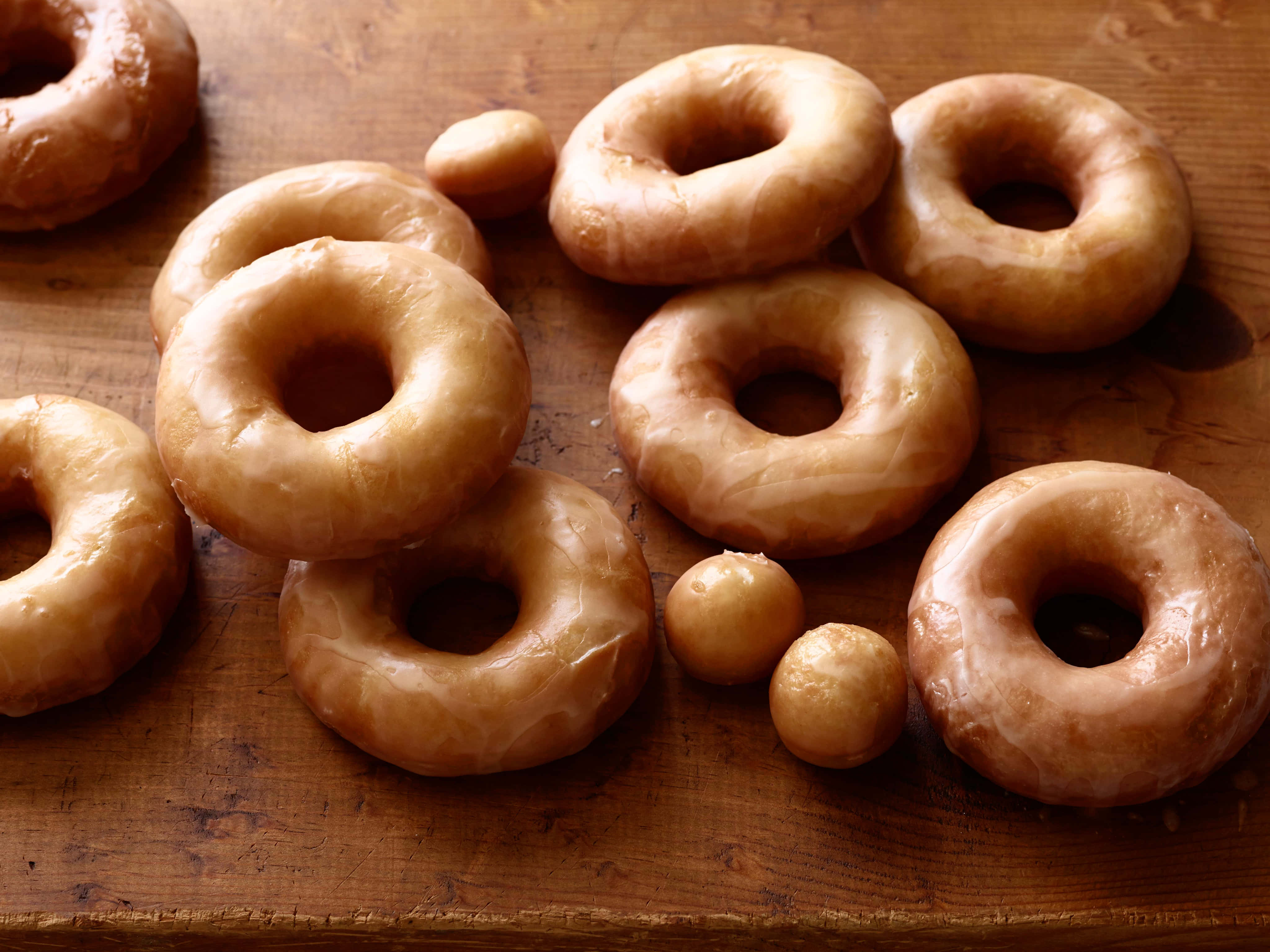 Glazed Donut 桌布 壁紙 — 金黃釉面甜甜圈和迷你甜甜圈在溫暖自然光下，誘人地放在質樸的木質表面上。
